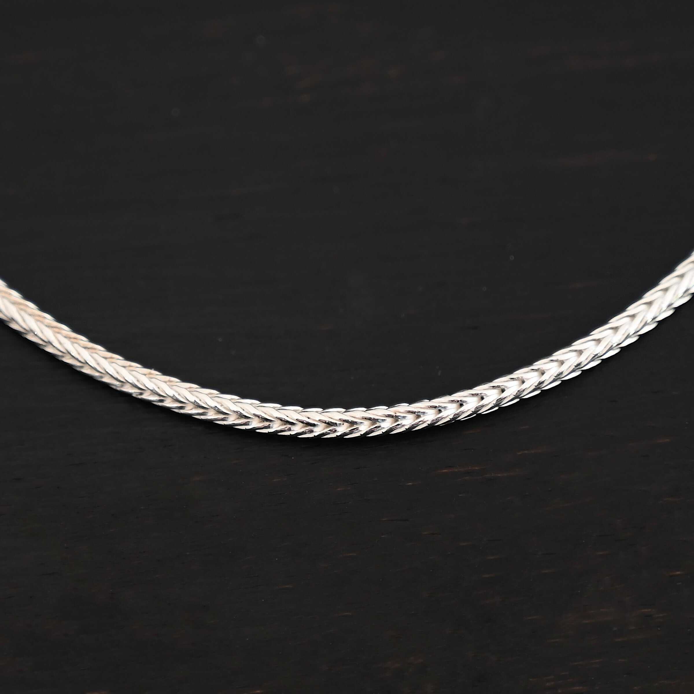 "Snake Foxtail" Chain. Chain is handmade out of sterling silver and woven together extremely tightly. Chain is shiny. Chain is laying against a dark background.