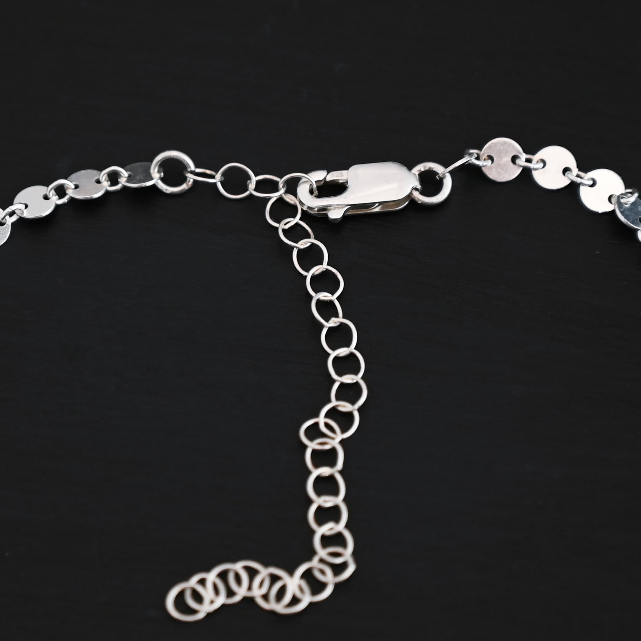 Clasp of the "Gypsy Coin" Chain that is shiny and sterling silver. It is a lobster claw clasp laying against a dark background with a 3 inch extension.