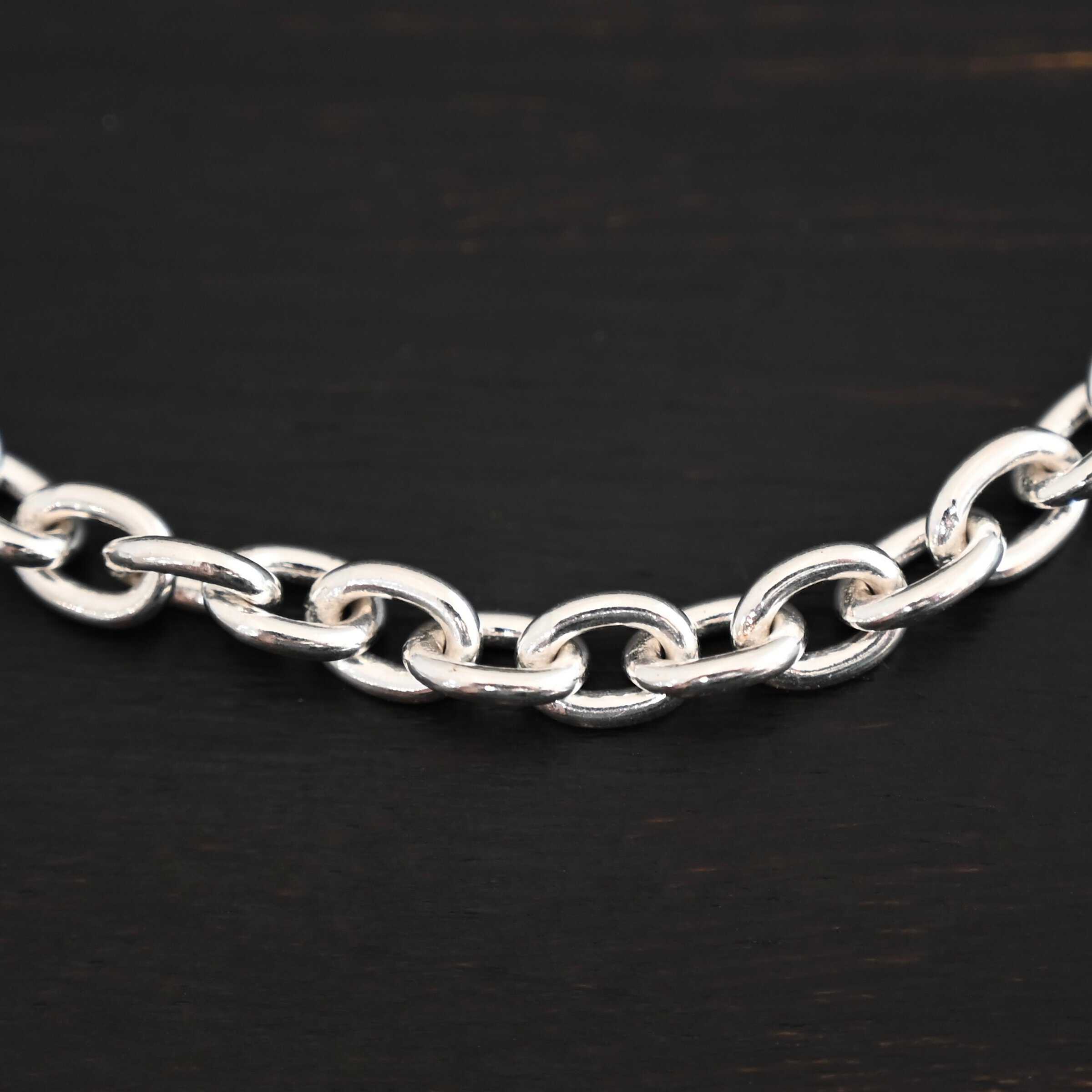 Close up of Georgia Chain that is shiny sterling silver and has thick oval links that measure 8x6mmx1.7mm thick. Chain is resting against a dark background.