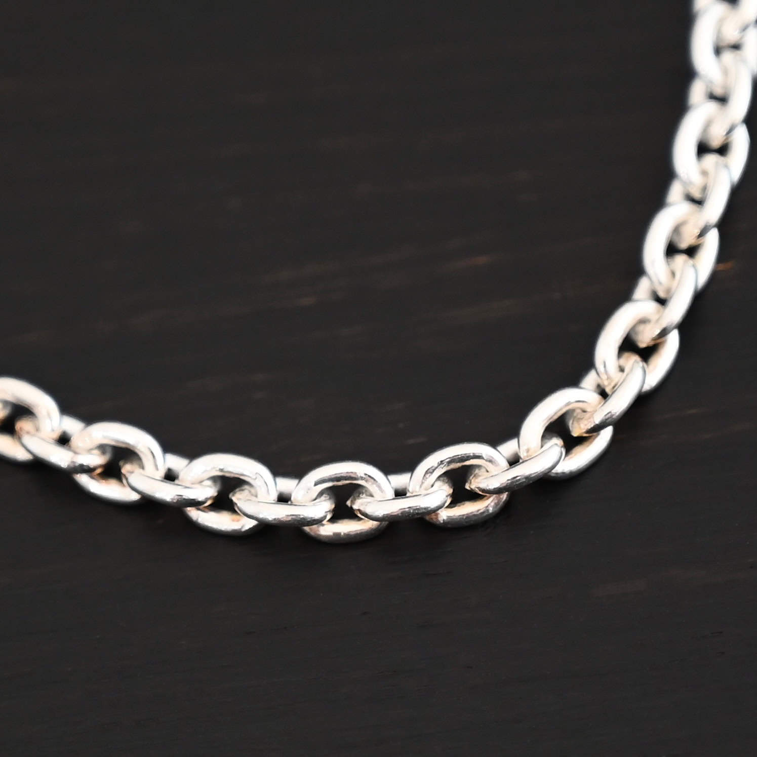 Joan Chain Shiny Close up of a Shiny sterling silver Joan chain with oval links that is resting against a dark background. Links are 6x5mmx1.2mm thick.