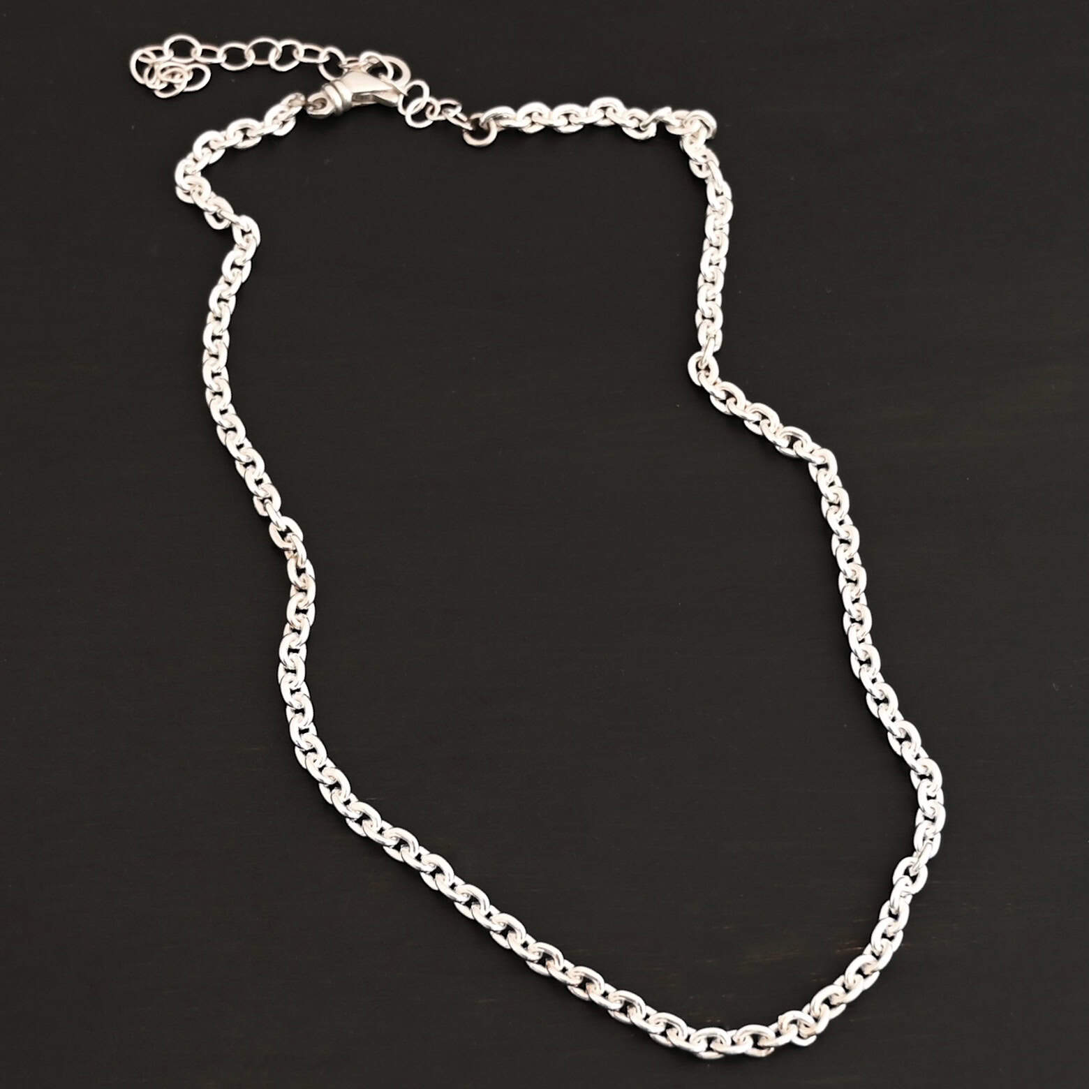 Joan Chain Shiny Shiny sterling silver Joan Chain with oval links that are 6x5mmx1.2mm thick that is laying on a dark background.