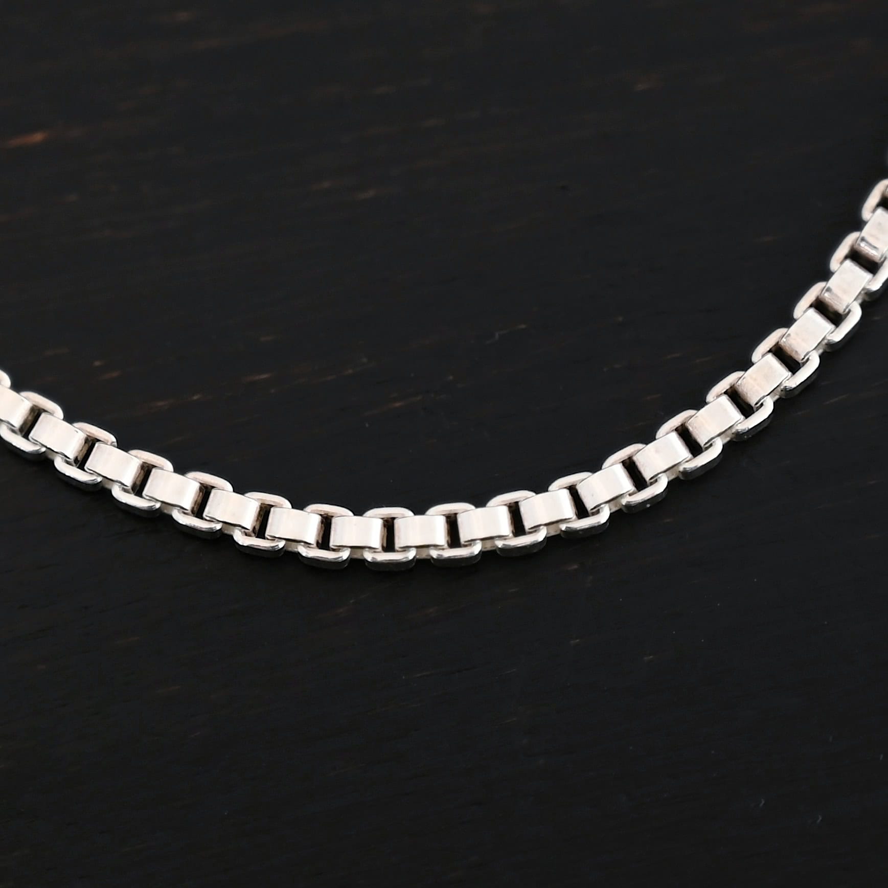 A close-up of the shiny sterling silver Briggs Box chain set against a dark black background