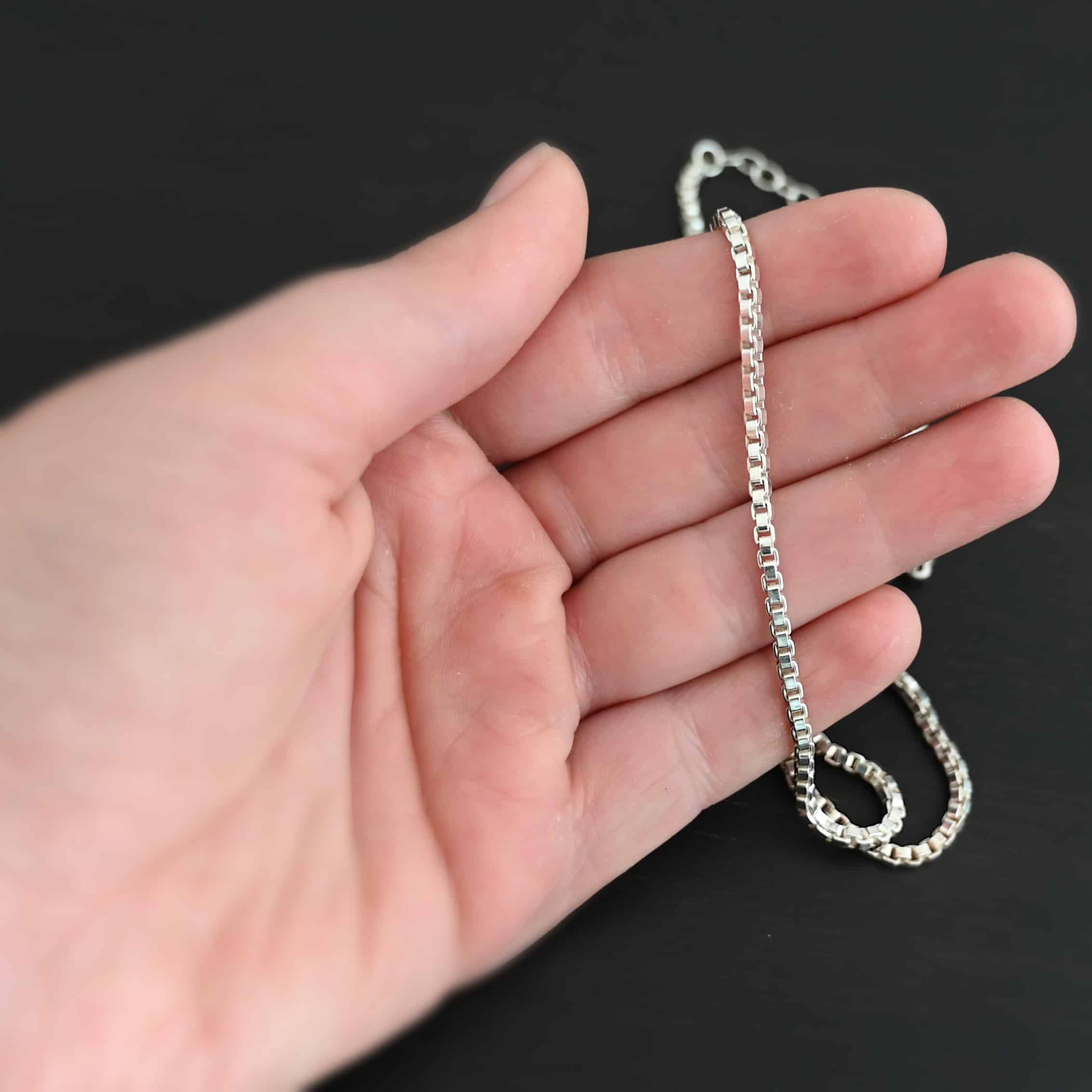 Shiny sterling silver Briggs Box chain set on a hand that is laying against a black background