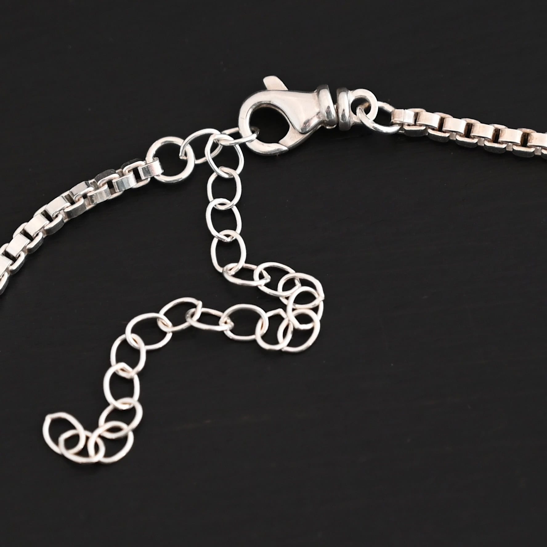 A close-up of the shiny sterling silver Briggs Box chain set against a dark black background with an emphasis on the lobster claw clasp that is on the chain