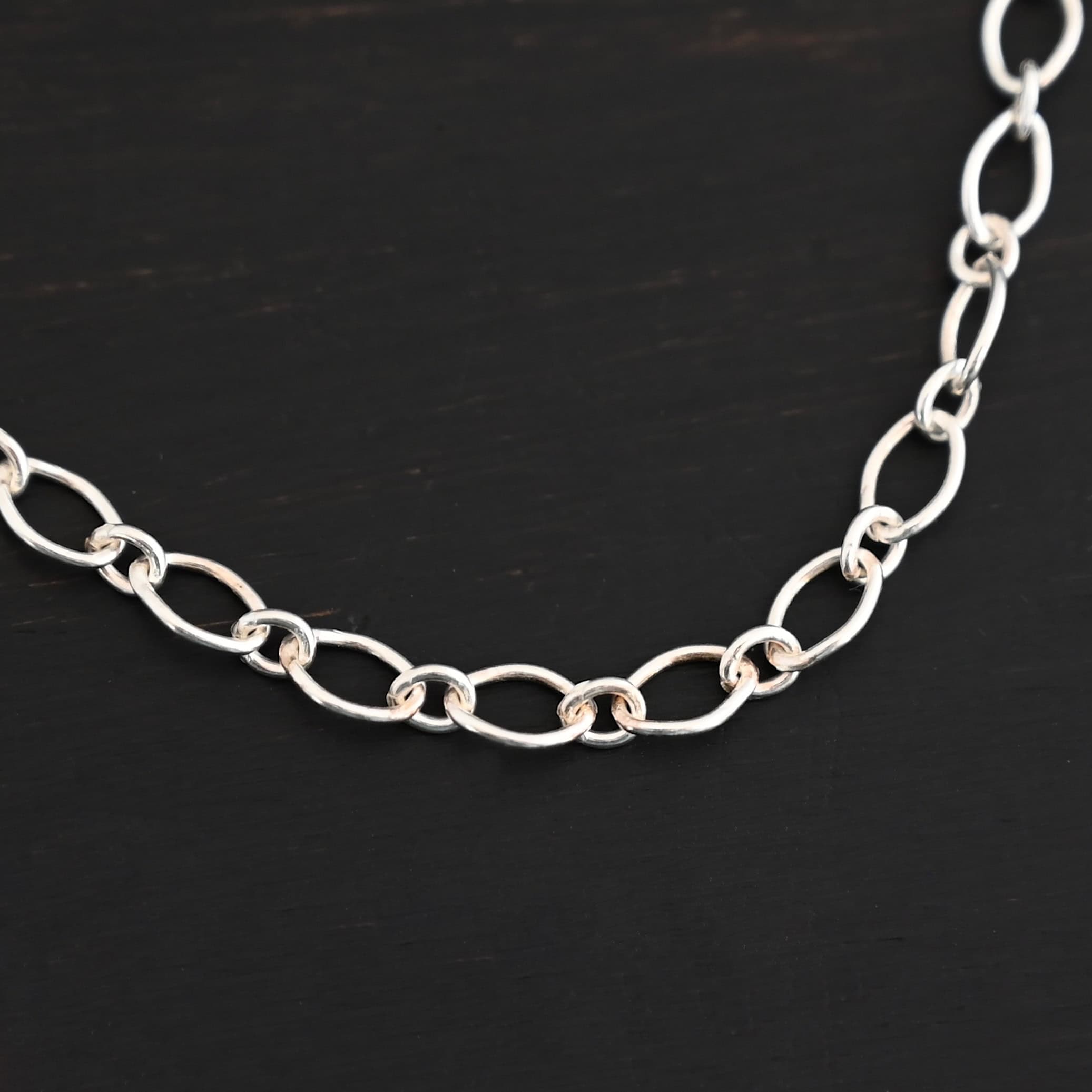 Allie Chain Shiny Shiny sterling silver Allie chain with links that alternate from circles to ovals laying against a dark background