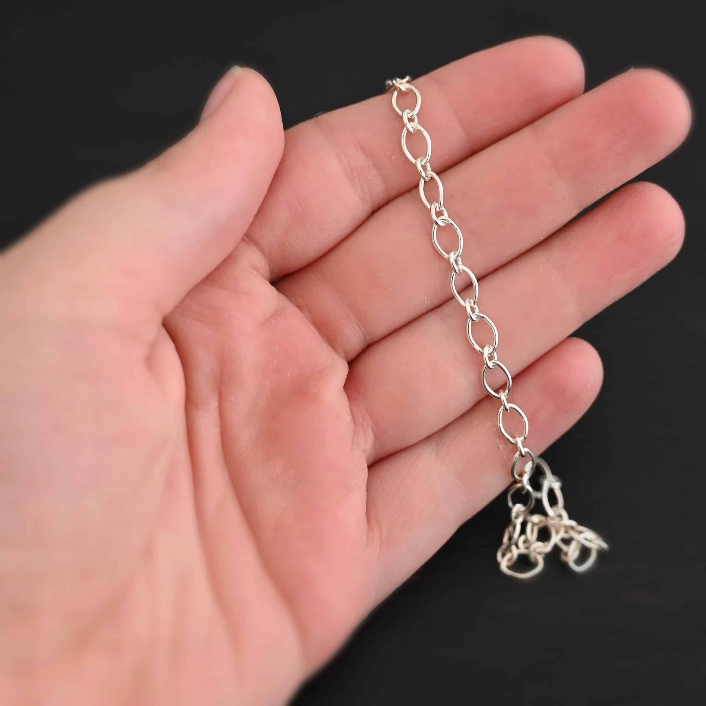 Allie Chain Shiny Shiny sterling silver Allie chain with oval links with circle jump rings holding them together lying against a hand that is resting on a dark background. Oval links measure 7×4.6mm for the chain.