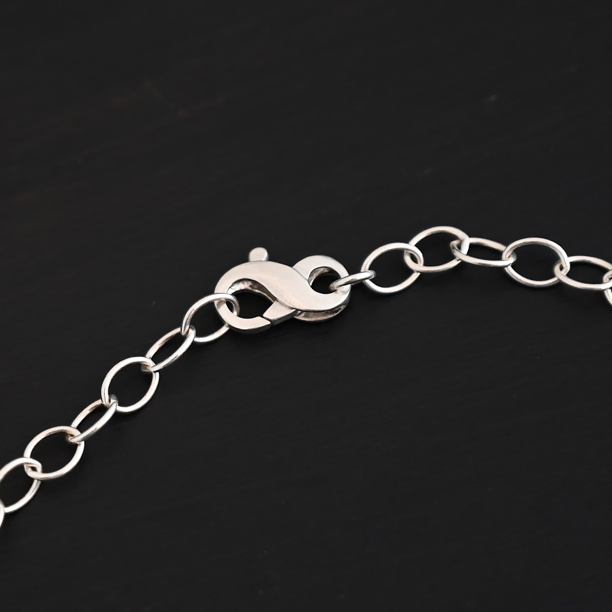 Willow Chain Shiny Shiny sterling silver Willow chain with oval links measuring 6.5×4.7mm. Chain is lying on a dark background with the infinity clasp showing as the main focus