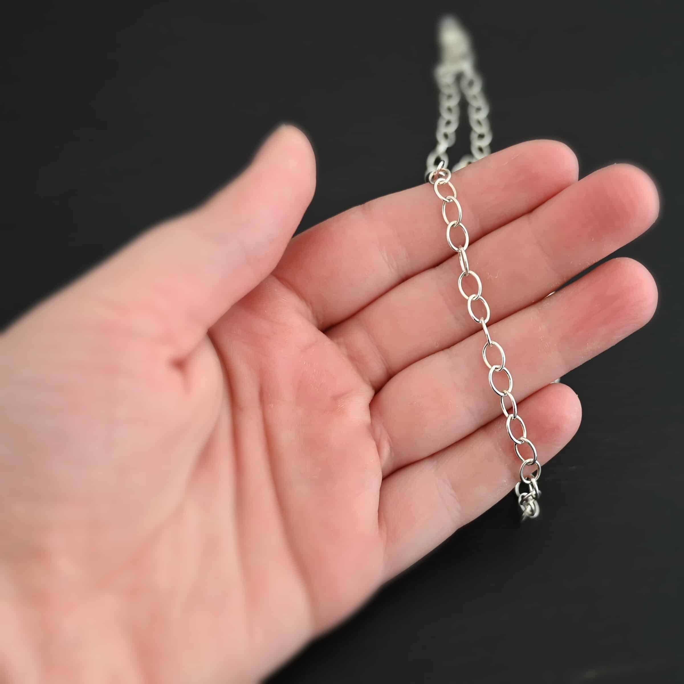 Willow Chain Shiny Sterling Silver Willow oval chain shown laying on a hand against a dark background. Oval links measure 6.5×4.7mm.