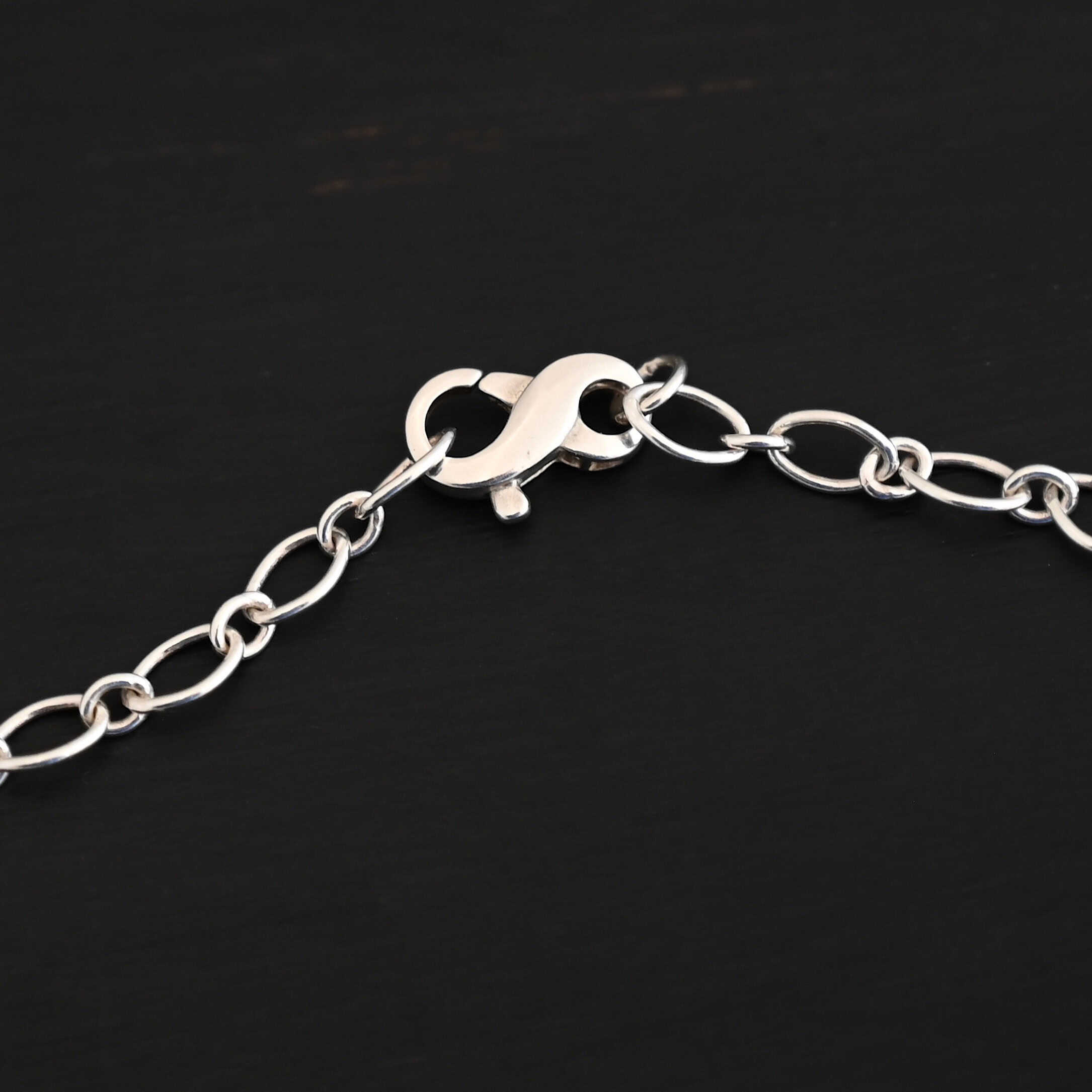 Allie Chain Shiny Shiny sterling silver Allie chain with alternating circle and oval links laying on a dark background with the infinity clasp showing as the main focus. Oval links measure 7×4.6mm for the chain.