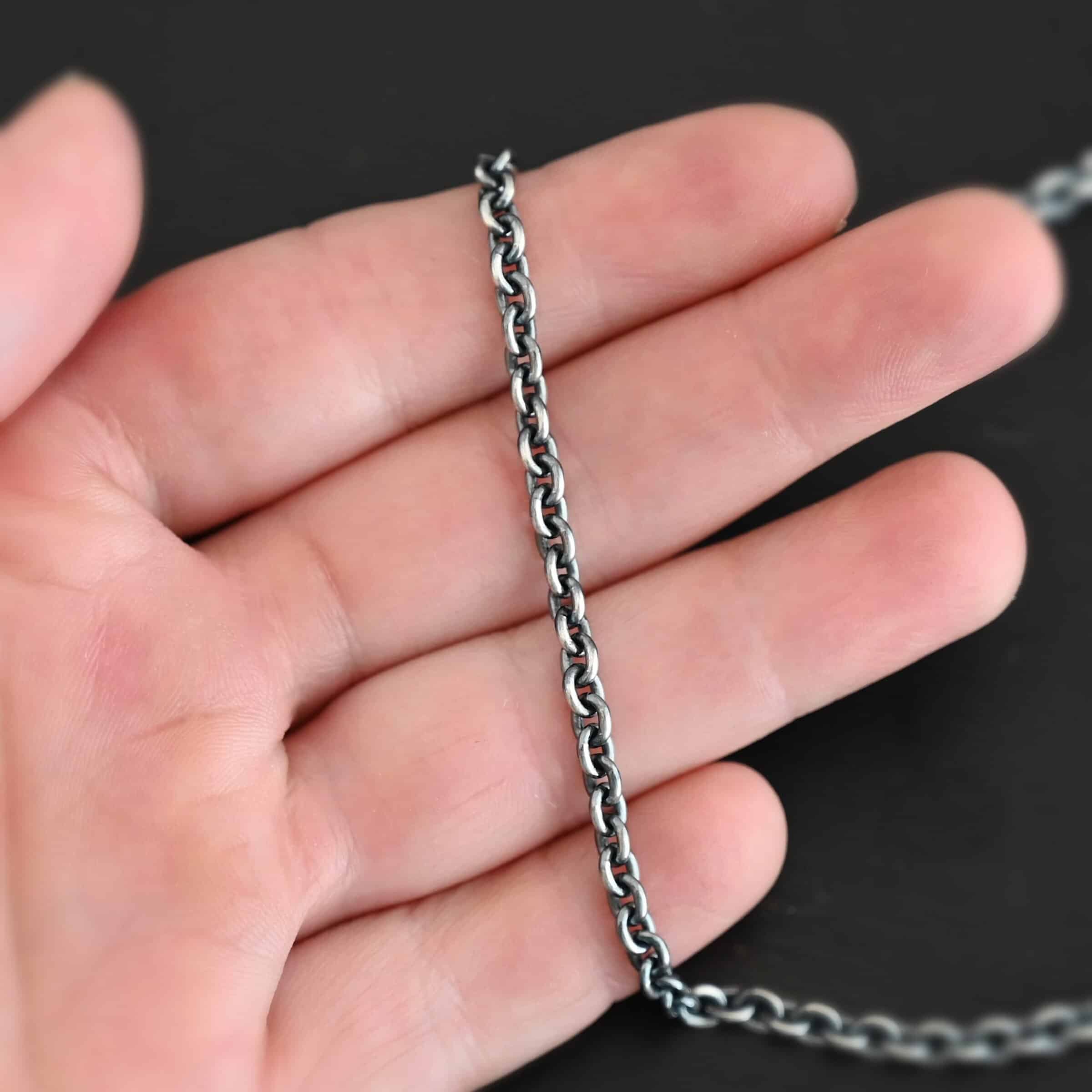 Close up of a oxidized sterling silver Lauren Chain with oval links that is laying on a hand that is resting against a dark background. Links measure 5x4mmx1mm thick.