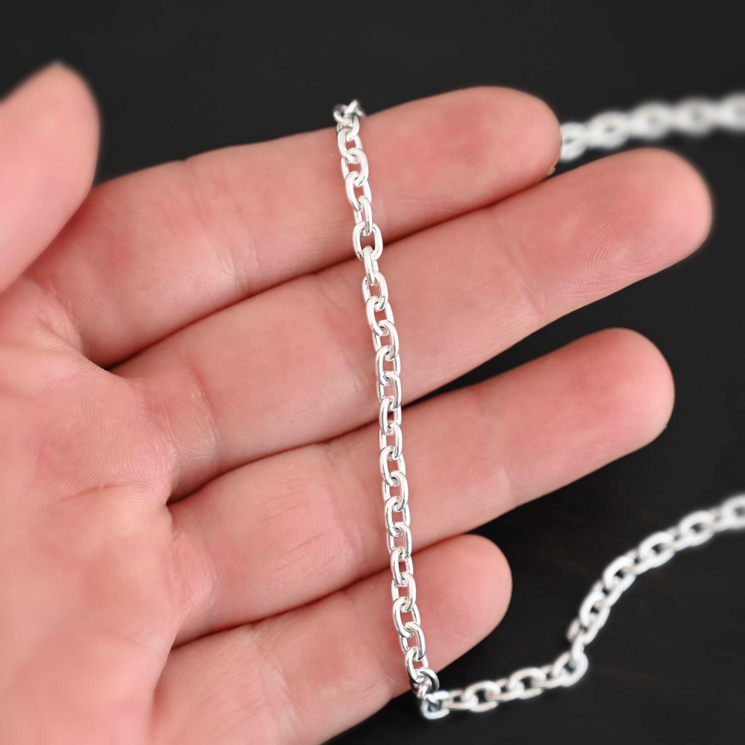 Close up of a shiny sterling silver Lauren Chain with oval links that is laying on a hand that is resting against a dark background. Links measure 5x4mmx1mm thick.