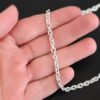 Shiny sterling silver Joan Chain with oval links that are 6x5mmx1.2mm thick lying against a hand that is resting on a dark background.