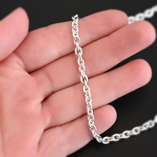Shiny sterling silver Joan Chain with oval links that are 6x5mmx1.2mm thick lying against a hand that is resting on a dark background.