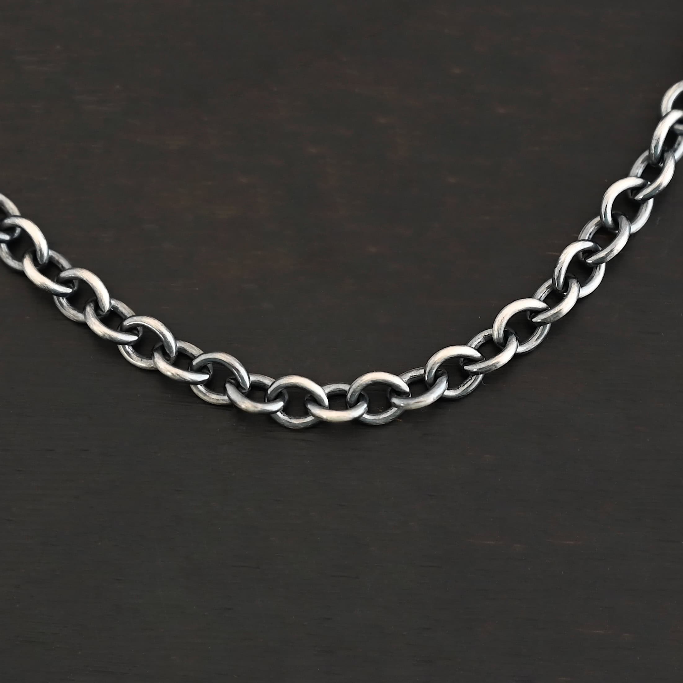 Close up of an oxidized sterling silver Joy chain with circular links laying on a dark background. Links measure 6.5×5.4mm.