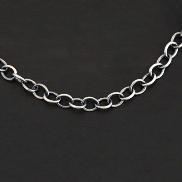 A close-up of the oxidized sterling silver Jay chain set against a dark black background. Links measure 7.2×5.7mm.