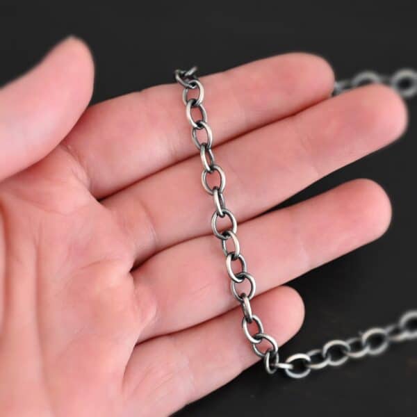 Oxidized sterling silver Jay chain with circular links that measure 7.2×5.7mm lying on a hand that is resting against a dark background.