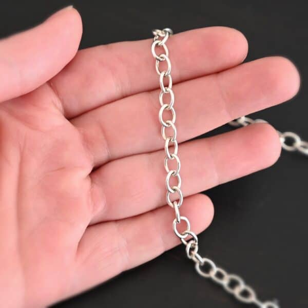 Shiny sterling silver Jay chain with circular links that measure 7.2×5.7mm lying on a hand that is resting against a dark background.