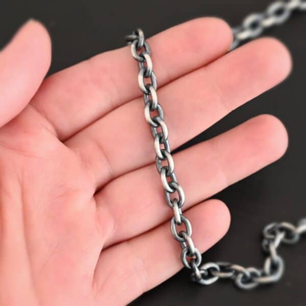 Oxidized sterling silver Georgia Chain with thick oval links that measure 8x6mmx1.7mm thick lying on a hand that is resting against a dark background.