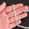 Shiny sterling silver Georgia Chain with thick oval links that measure 8x6mmx1.7mm thick lying on a hand that is resting against a dark background.