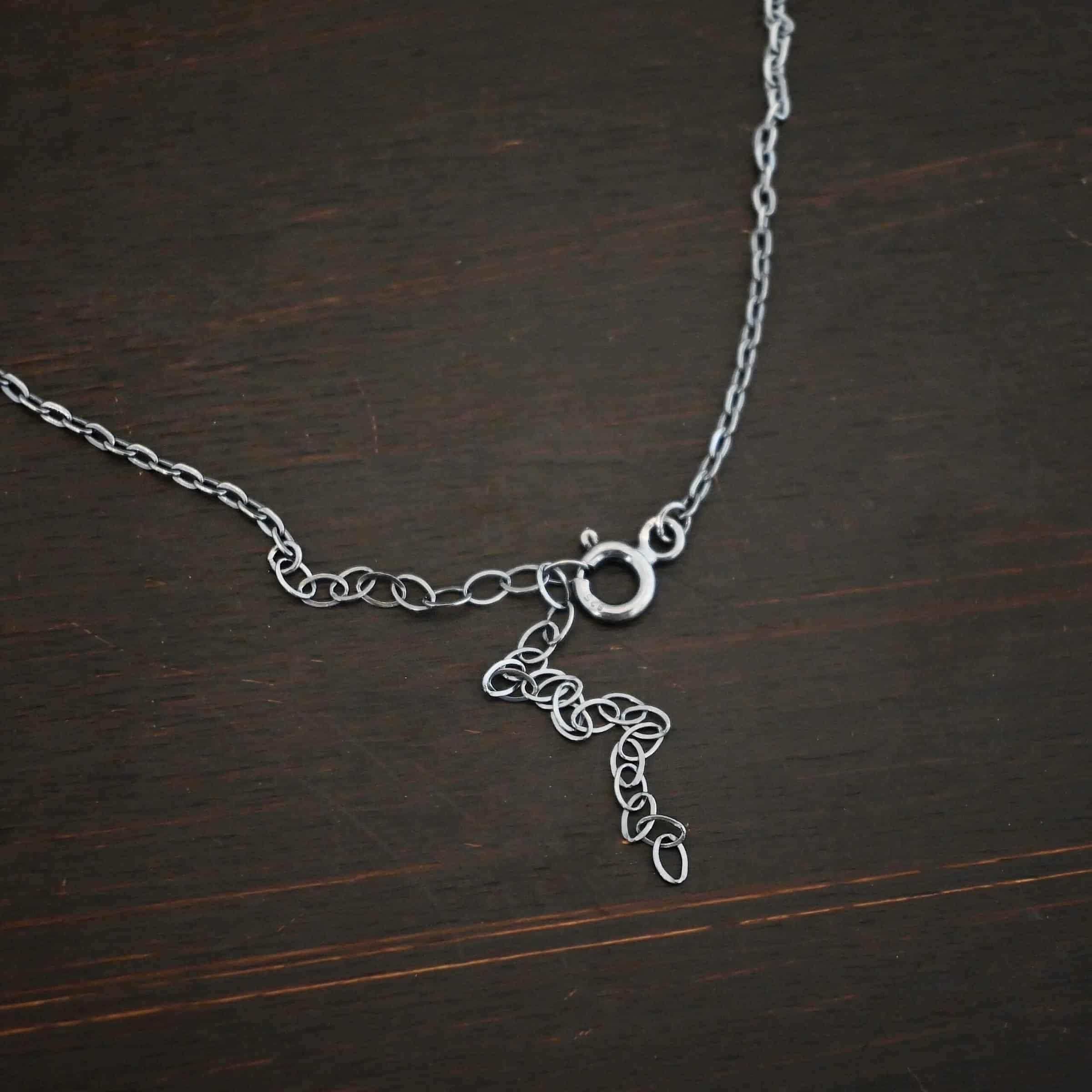 Cassandra Chain "Cassandra" Chain as shown lying against a dark background. Chain is shown as oxidized. Chain has 2x2mm links. Chain has a spring ring clasp that is the primary focus of the photo.