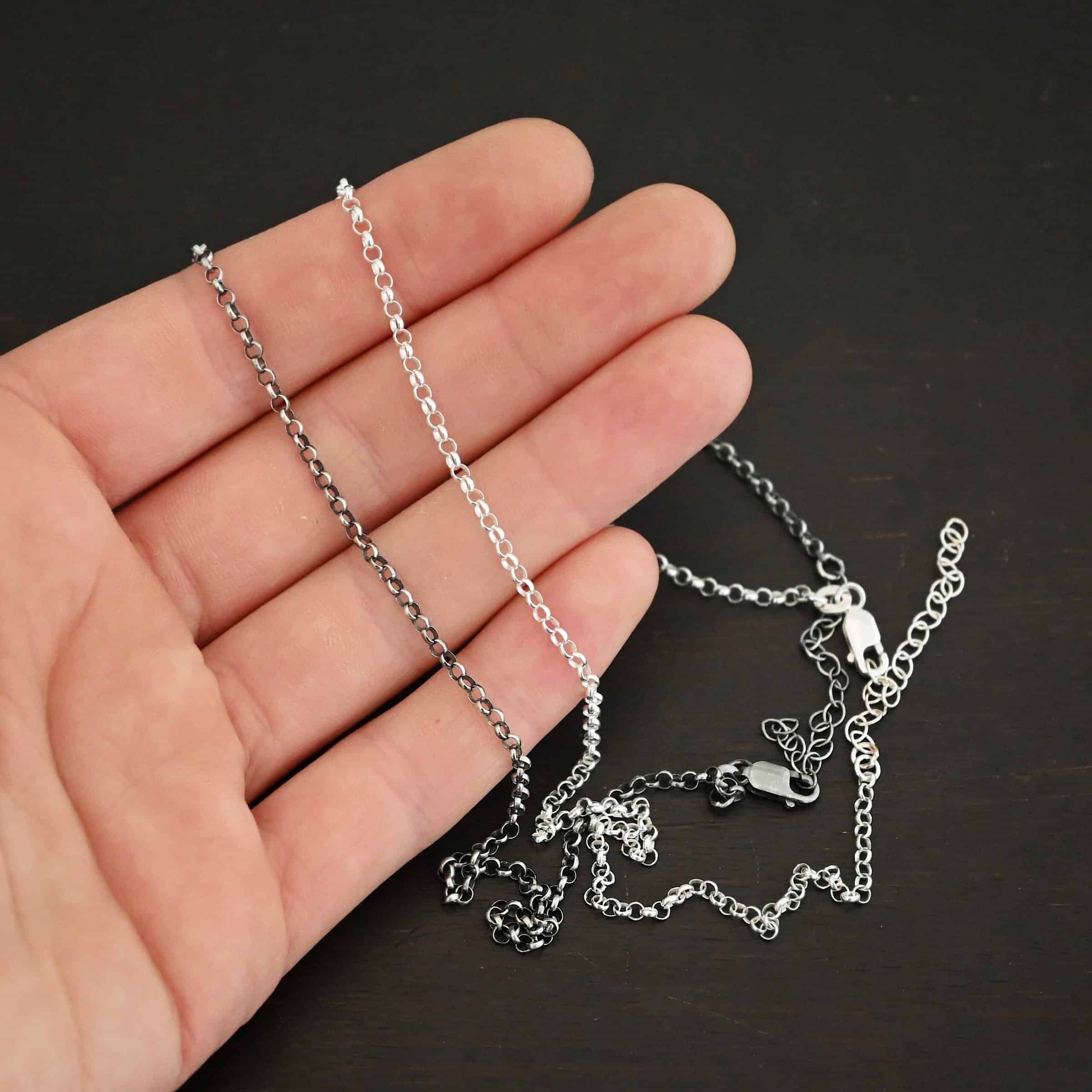 "Rachel Rolo" Chain as shiny and oxidized. Made out of sterling silver. Chain is made out of small, but thick circles that are connected to one another. The oxidized chain is on the top and shiny on the bottom. Chain is lying against the fingertips of a hand.