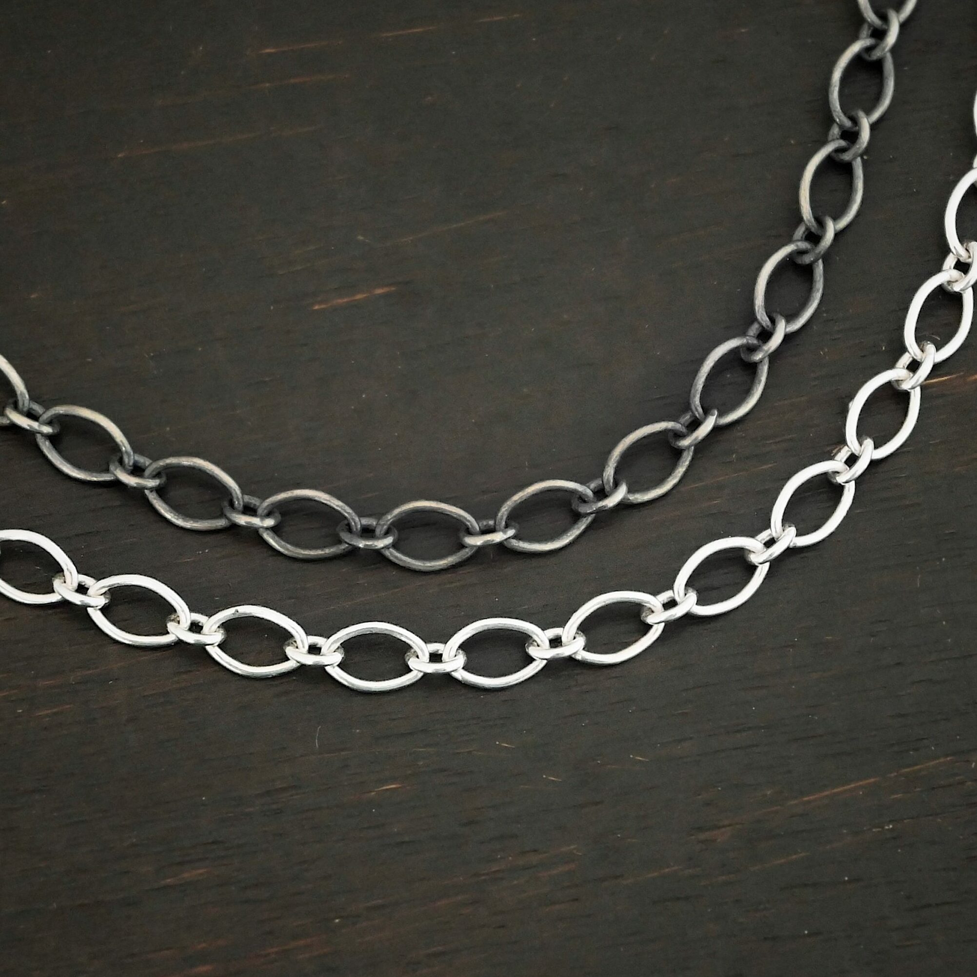 Allie Chain "Allie" Chain as shown as both shiny and oxidized up close. Oxidized is on top and the shiny chain is on the bottom. Oval links measure 7×4.6mm. Chains are shown against a dark background.