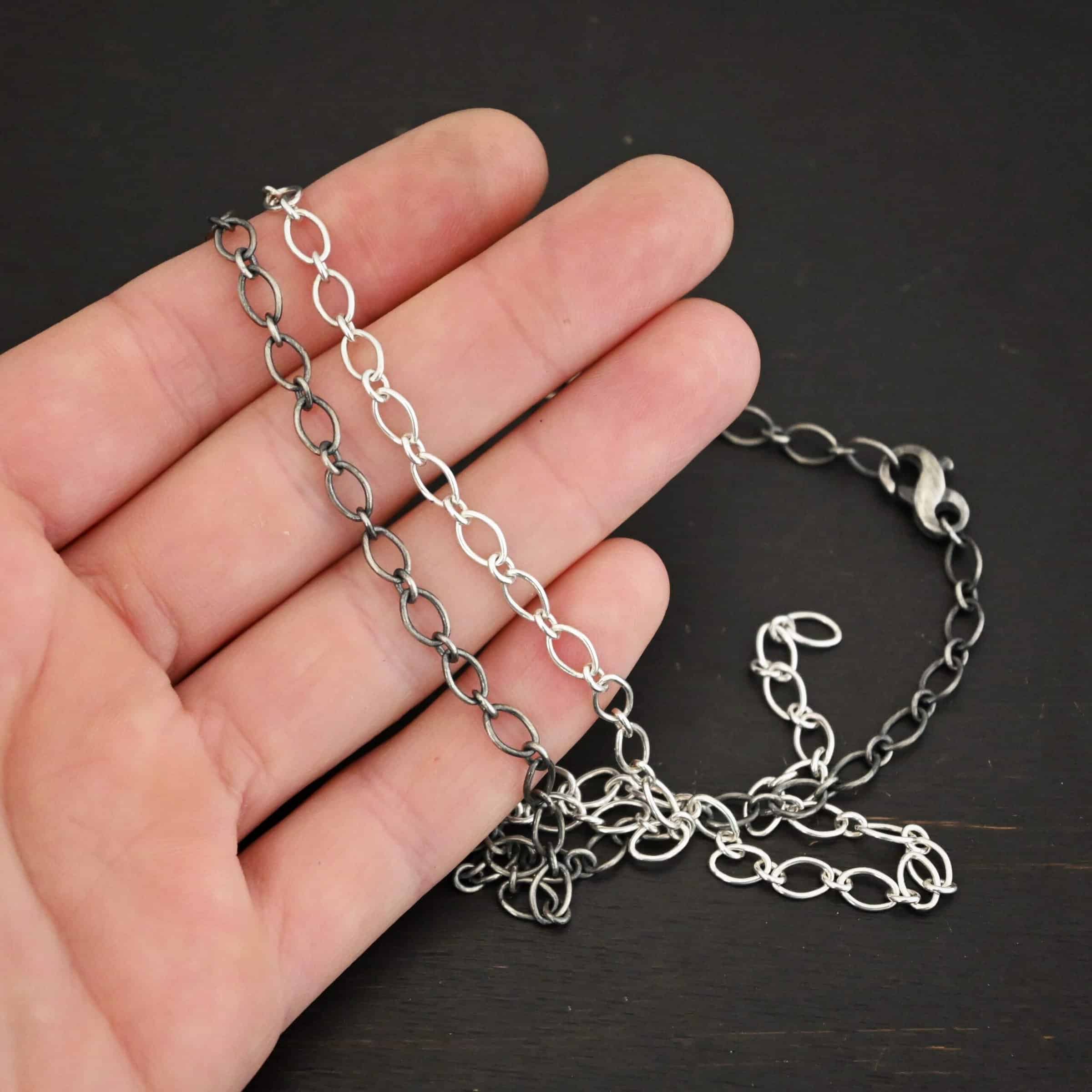 Allie Chain Shiny and oxidized sterling silver Allie chain with oval links with circle jump rings holding them together lying against a hand that is resting on a dark background. Oval links measure 7×4.6mm for the chain.