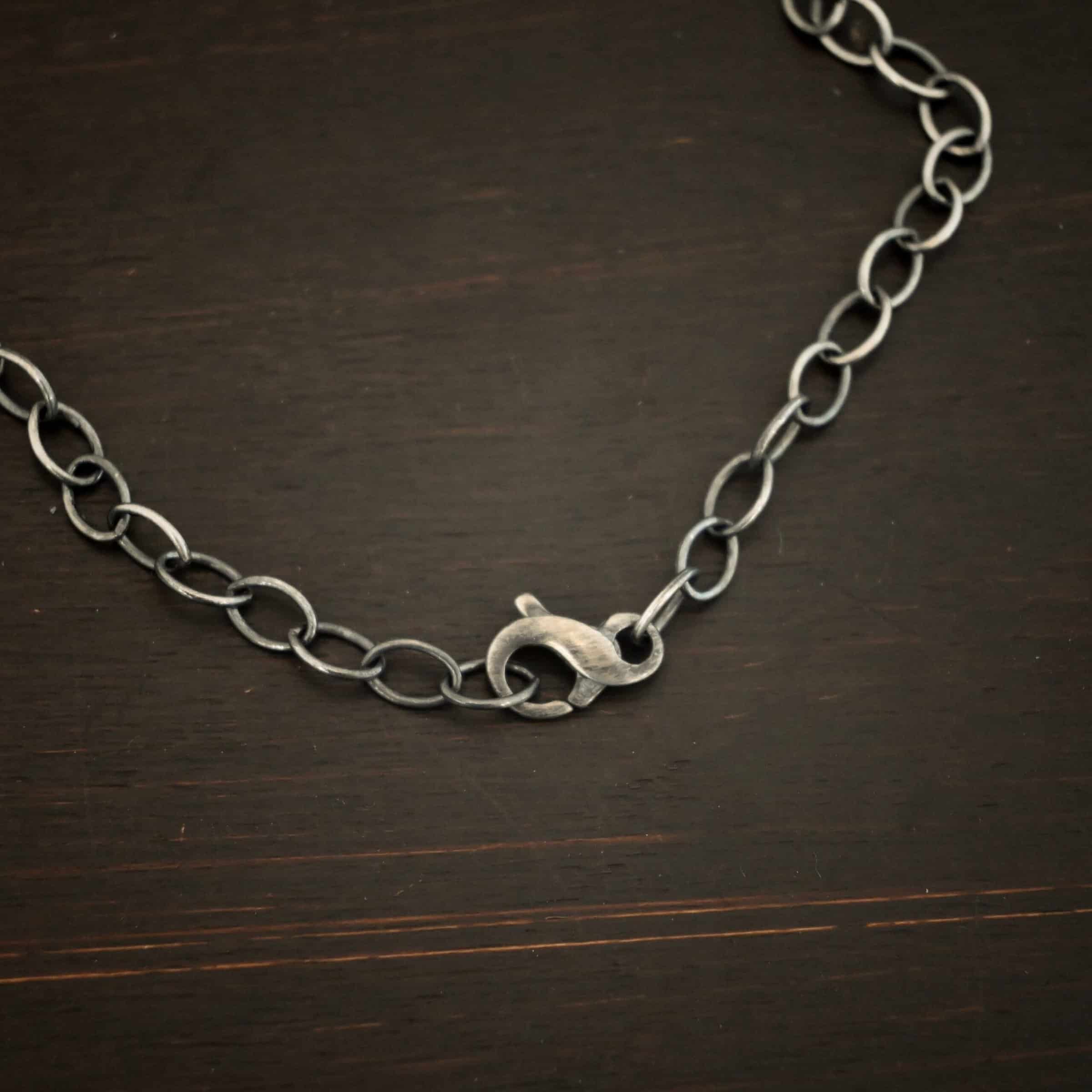 Willow Chain Oxidized sterling silver Willow chain with oval links measuring 6.5×4.7mm. Chain is lying on a dark background with the infinity clasp showing as the main focus