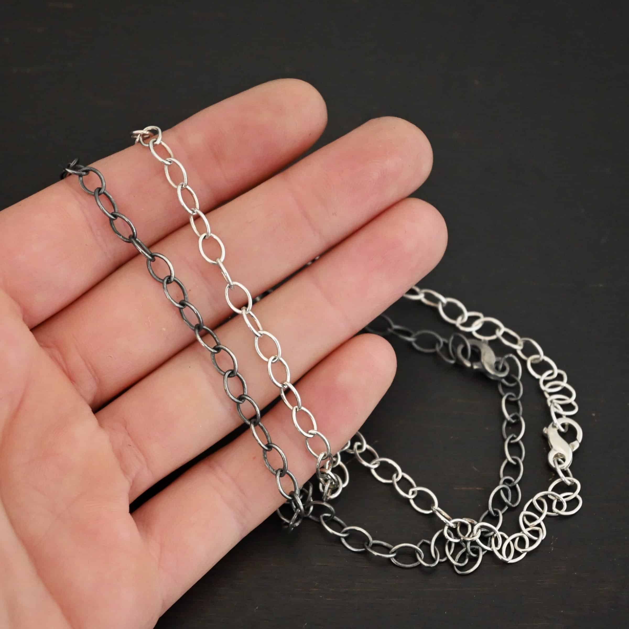 Willow Chain Sterling Silver Willow oval chain shown laying on a hand against a dark background. Oval links measure 6.5×4.7mm. Chain is shown as shiny and oxidized