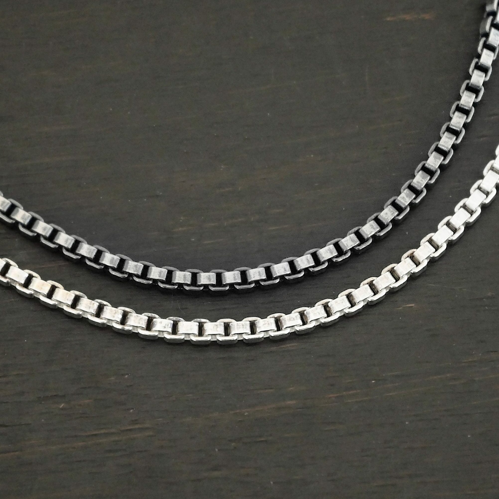 Close up of the "Briggs Box" Chain as both shiny and oxidized. Chain is made out of sterling silver and has box links that make up the chain. The chains are set up against the dark background. Heavy Box Chain 2.5mmx1.4mm.