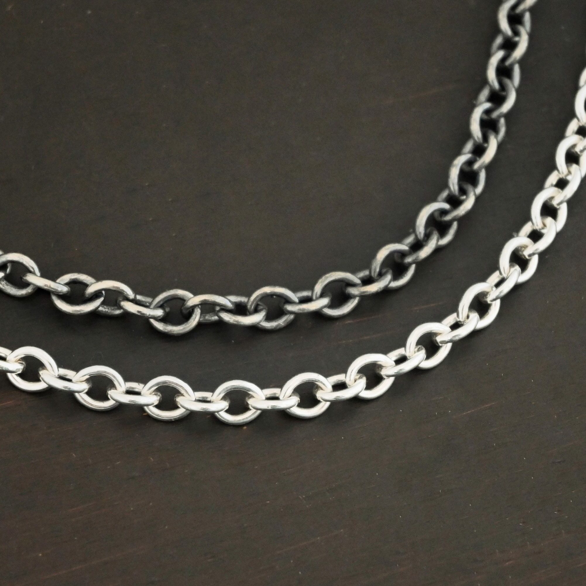 Close up of the "Joy" Chain as both shiny and oxidized. The Joy chain is made out of sterling silver and has heavy oval links that measure 6.5×5.4mm. The oxidized chain is on top and the shiny one is on the bottom. Chains are set against a dark background.