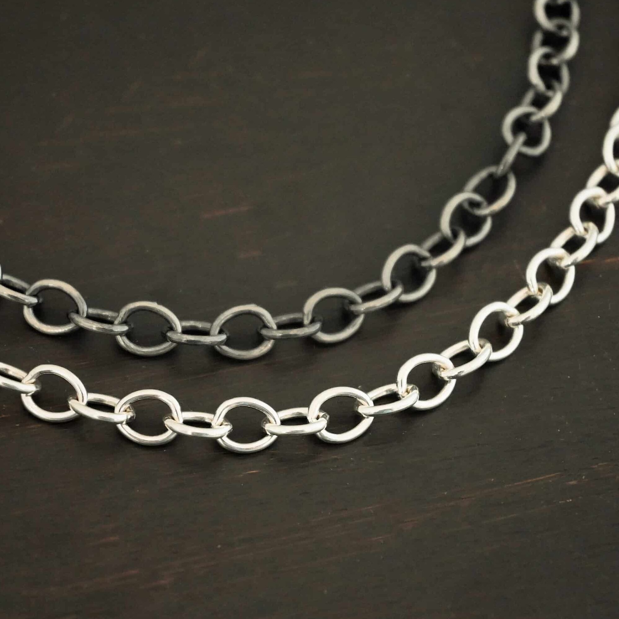 Jay Chain Close up of the "Jay" Chain shown as both shiny and oxidized. This chain is made out of sterling silver, and heavy oval links measure 7.2×5.7mm. Chain is shown laying against a dark background.