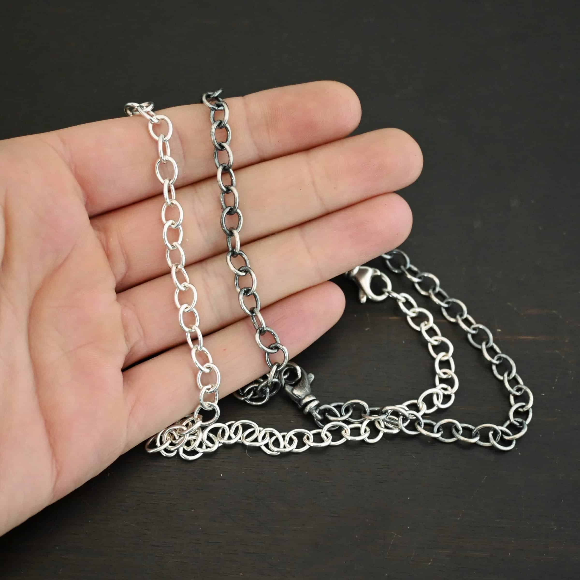 Jay Chain Shiny and oxidized sterling silver Jay chain with circular links that measure 7.2×5.7mm lying on a hand that is resting against a dark background.