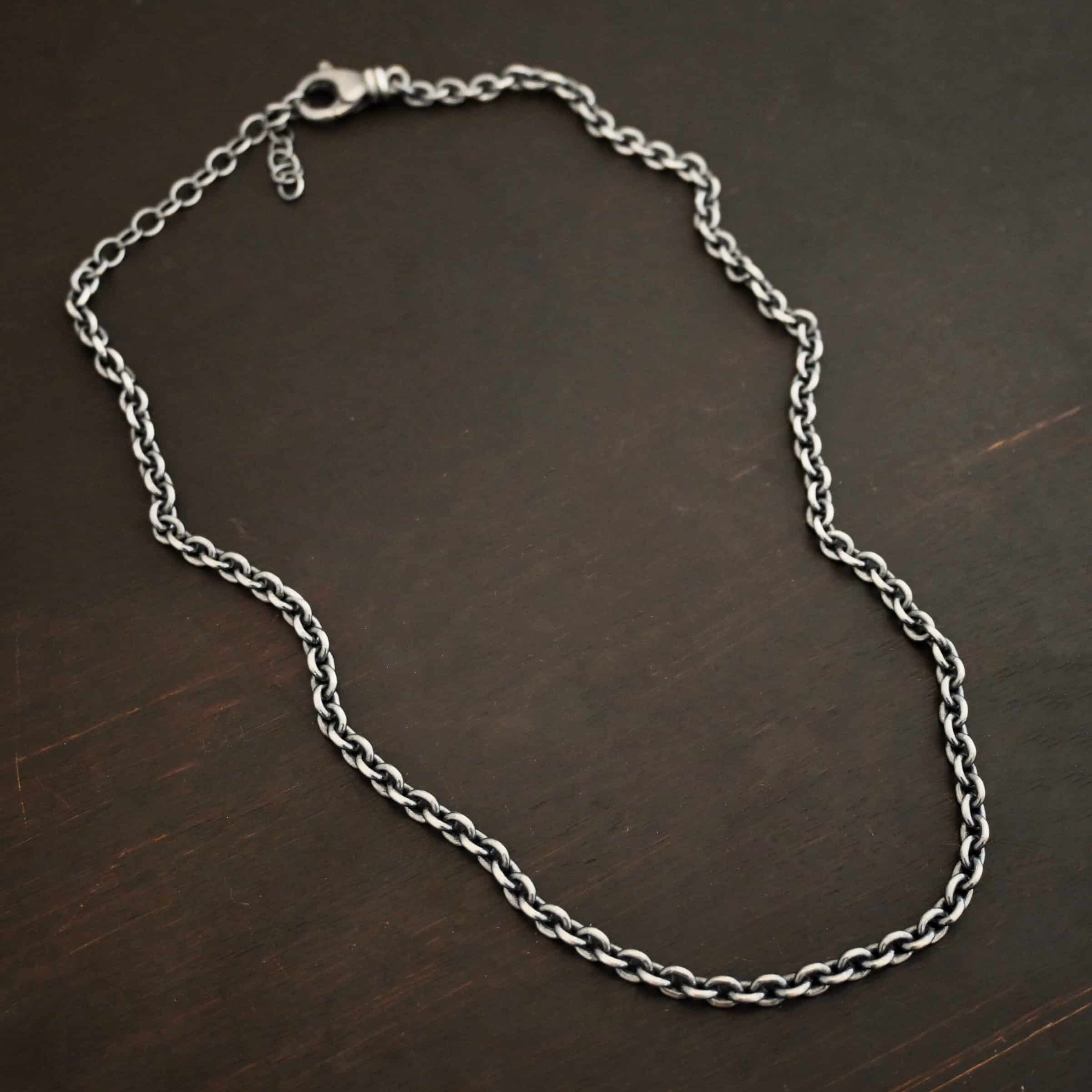 Joan Chain Oxidized sterling silver Joan Chain with oval links that are 6x5mmx1.2mm thick. Chain is lying on a dark background.