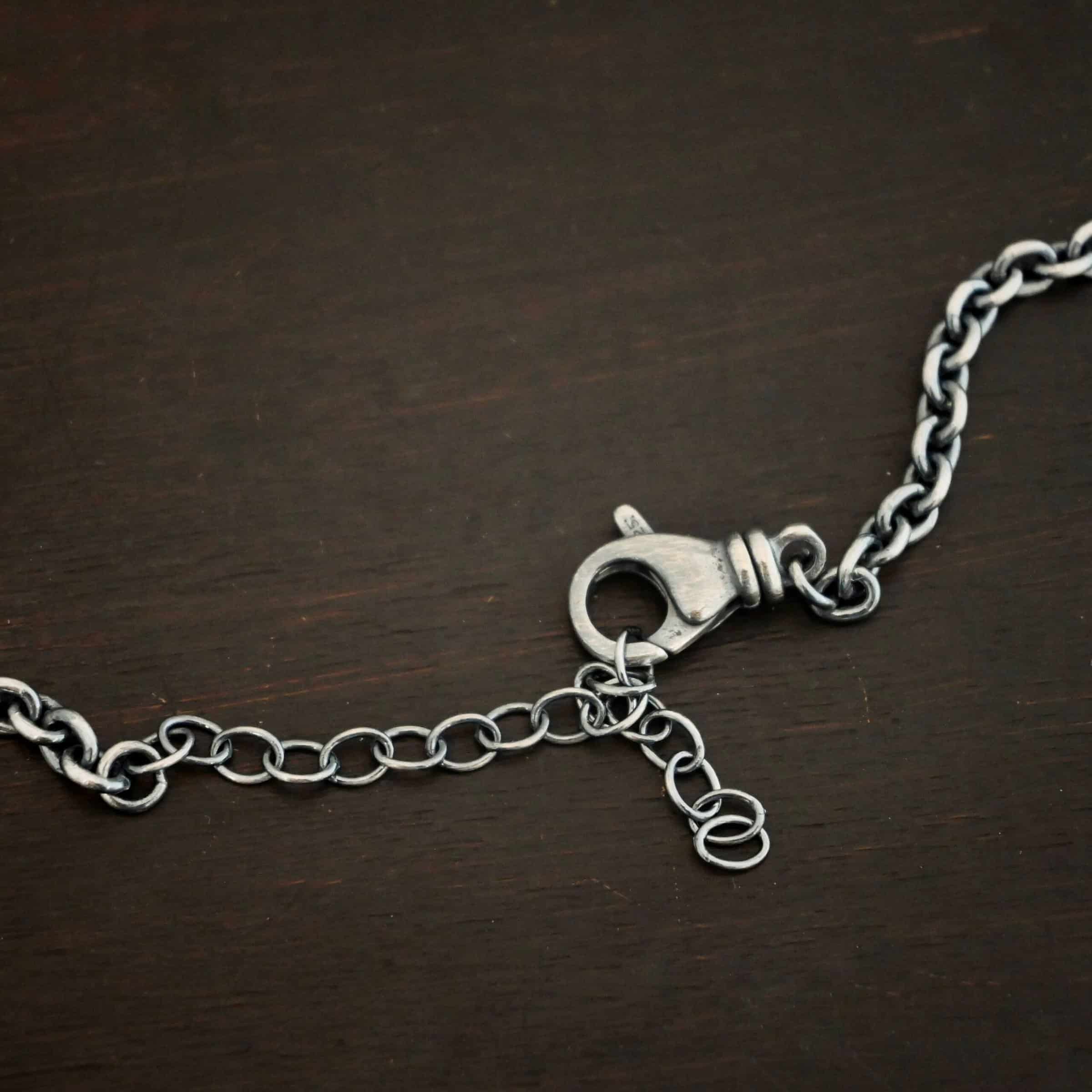Joan Chain Close up of an oxidized lobster claw clasp that is on an oxidized sterling silver Joan Chain with oval links that are 6x5mmx1.2mm thick that is laying on a dark background.