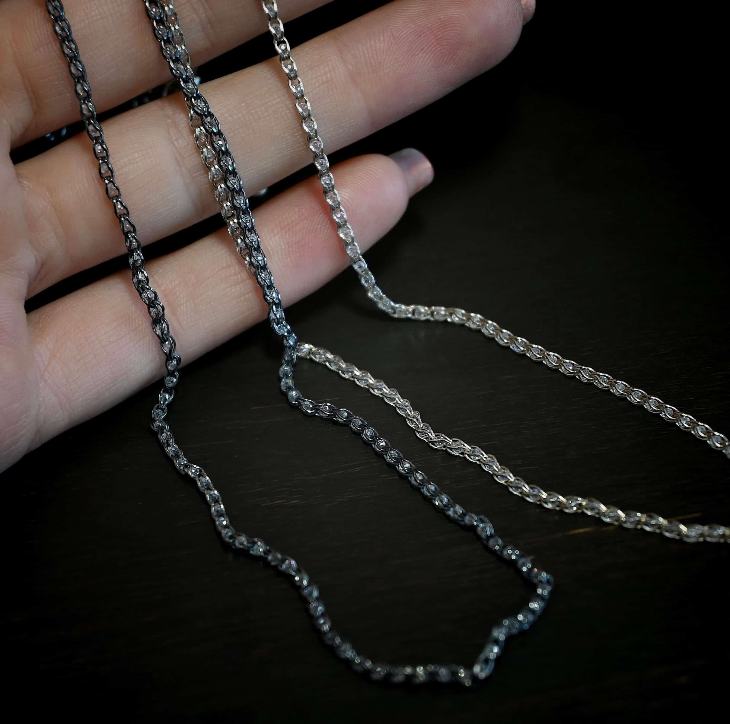 Scarlett Chain "Scarlett" Chain as shown up close and as both shiny and oxidized. Made out of sterling silver and has small cz's embedded in the chain with silver wrapped around them. Chain is shown against the fingertips of a hand.