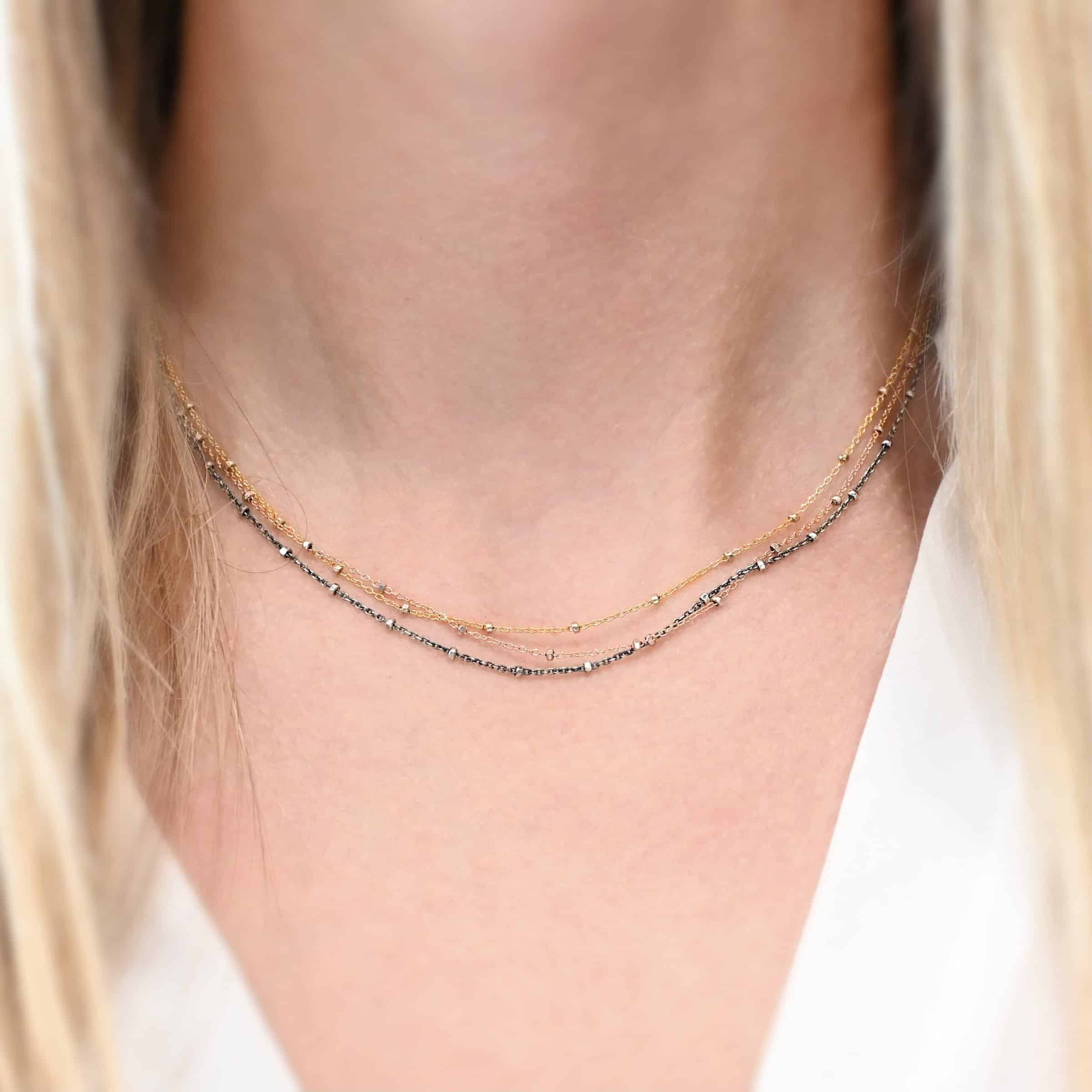 Champagne In Paris Necklace "Champagne In Paris" Chain as shown on a model at 16" long. Oxidized sterling silver, 14K Rose Gold Filled, & 14K Yellow Gold Filled Chain that is 1.2mm thick. Model is wearing a white v-neck shirt.