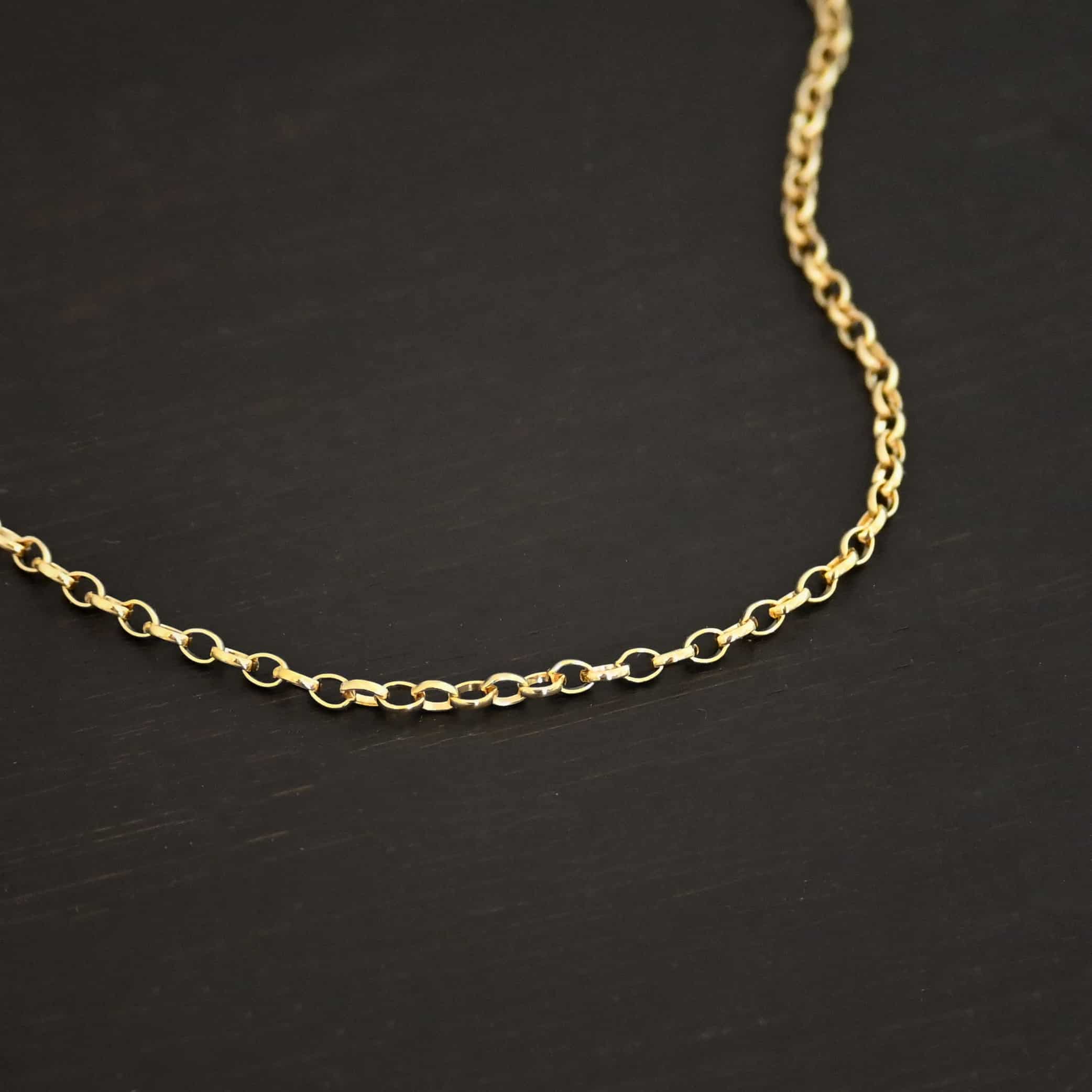 "Ruby Rolo" Chain as shown up close against a dark background. 14K Gold Filled over sterling silver with small circular links connected together. Chain is shown against a dark background.