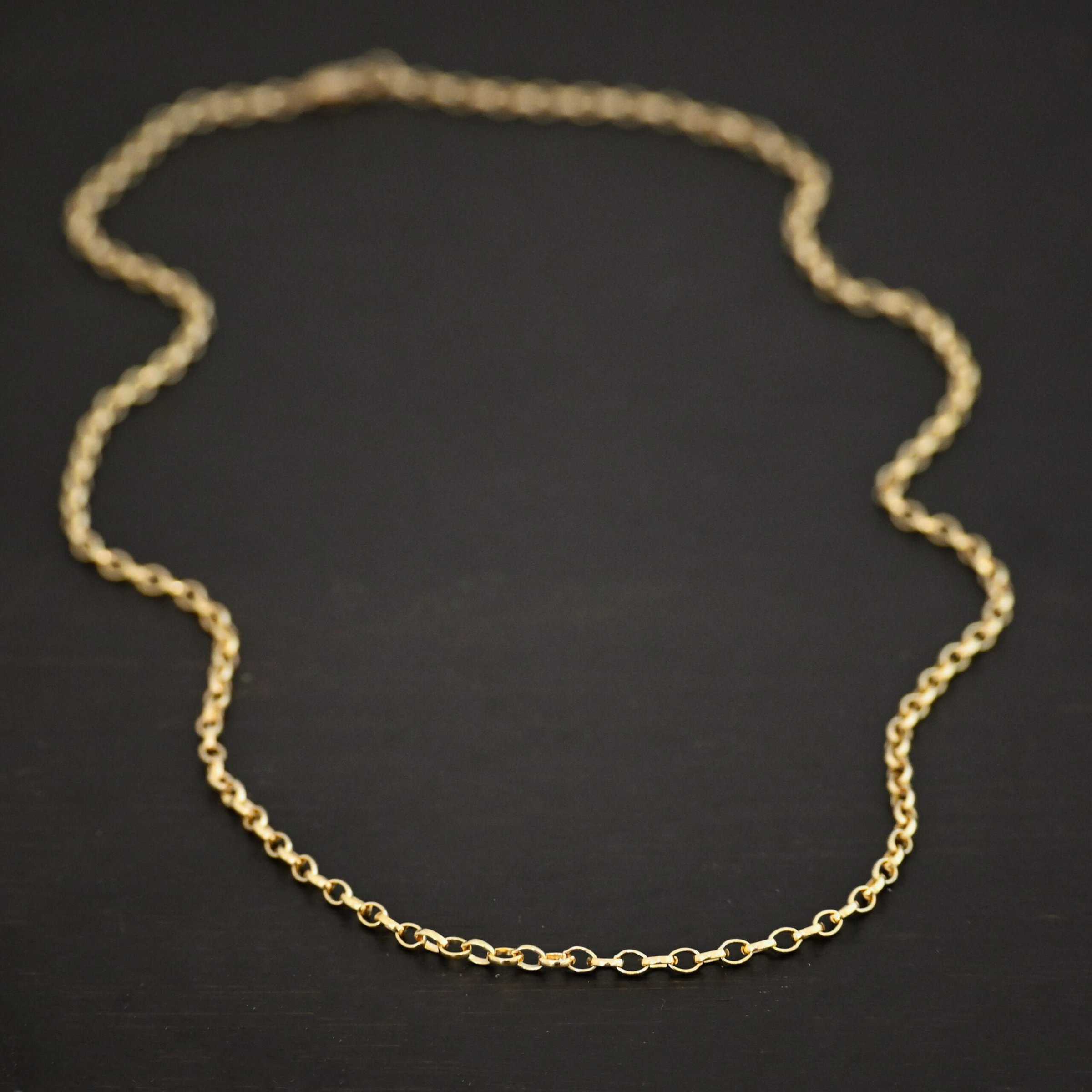 "Ruby Rolo" Chain as shown up close against a dark background. 14K Gold Filled over sterling silver with small circular links connected together. Chain is shown against a dark background.
