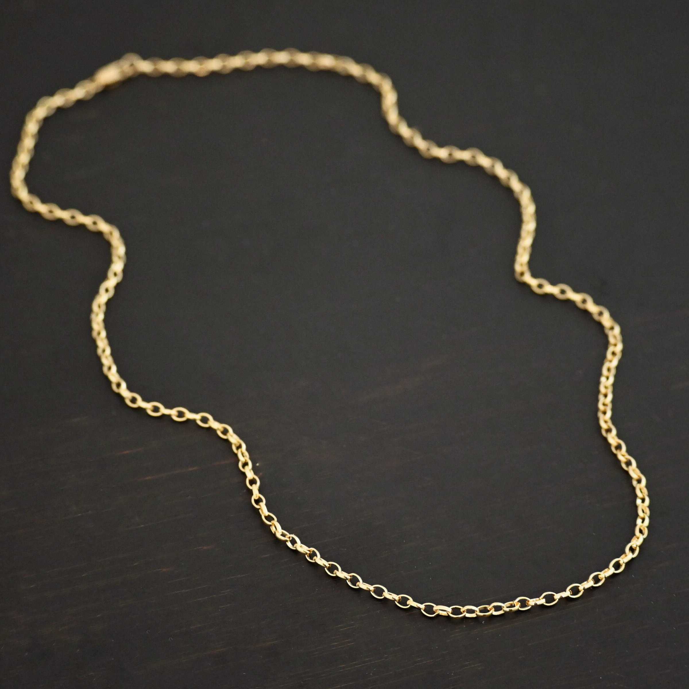 "Ruby Rolo" Chain as shown up close against a dark background. 14K Gold Filled over sterling silver with small circular links connected together. Chain is shown against a dark background.