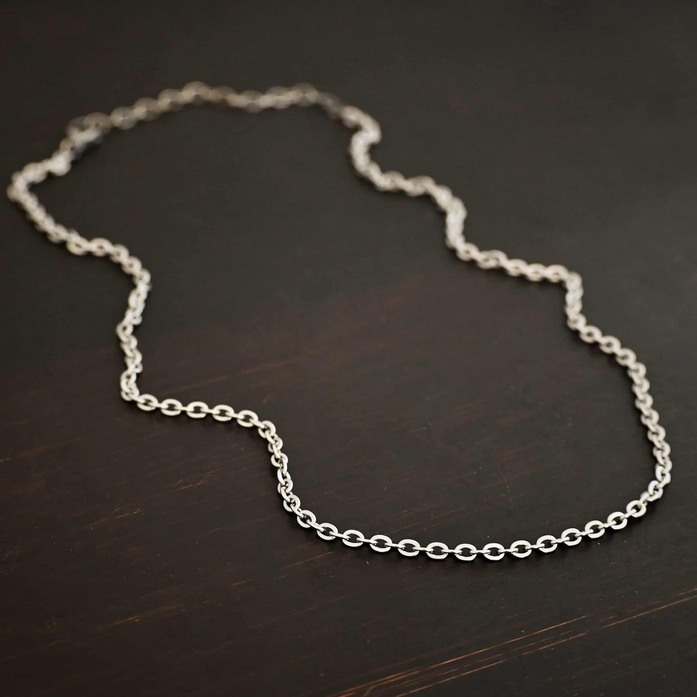 Simon Chain "Simon" Chain as shown up close. 4x3mm links and made out of stainless steel. Chain is laying against a dark background.