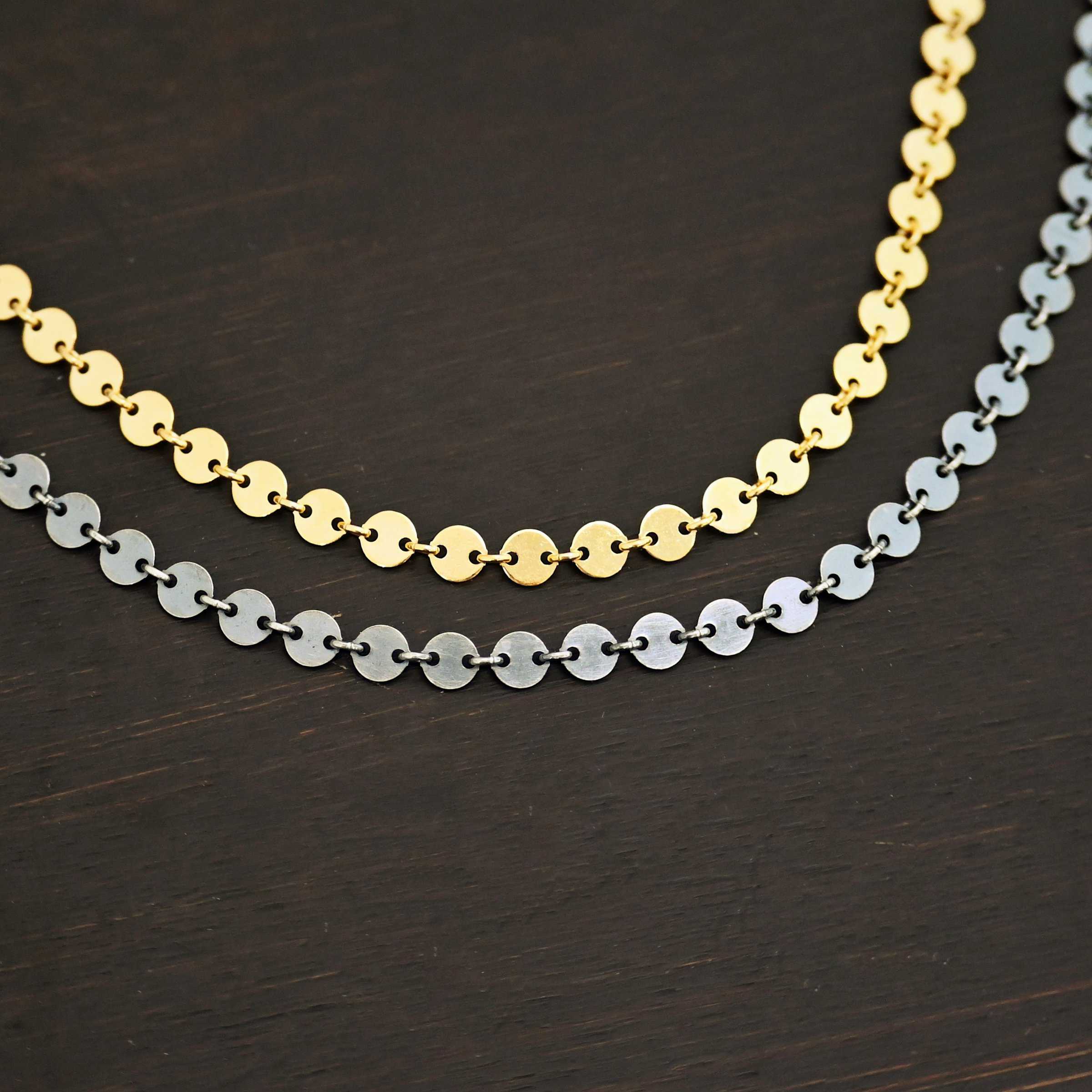 "Gypsy Coin" Chain as shown up close with gold filled and oxidized sterling silver. 4mm coin disks connected with jump rings. The gold filled chain is on top, and oxidized sterling silver is on the bottom. Chains are shown against a dark background.