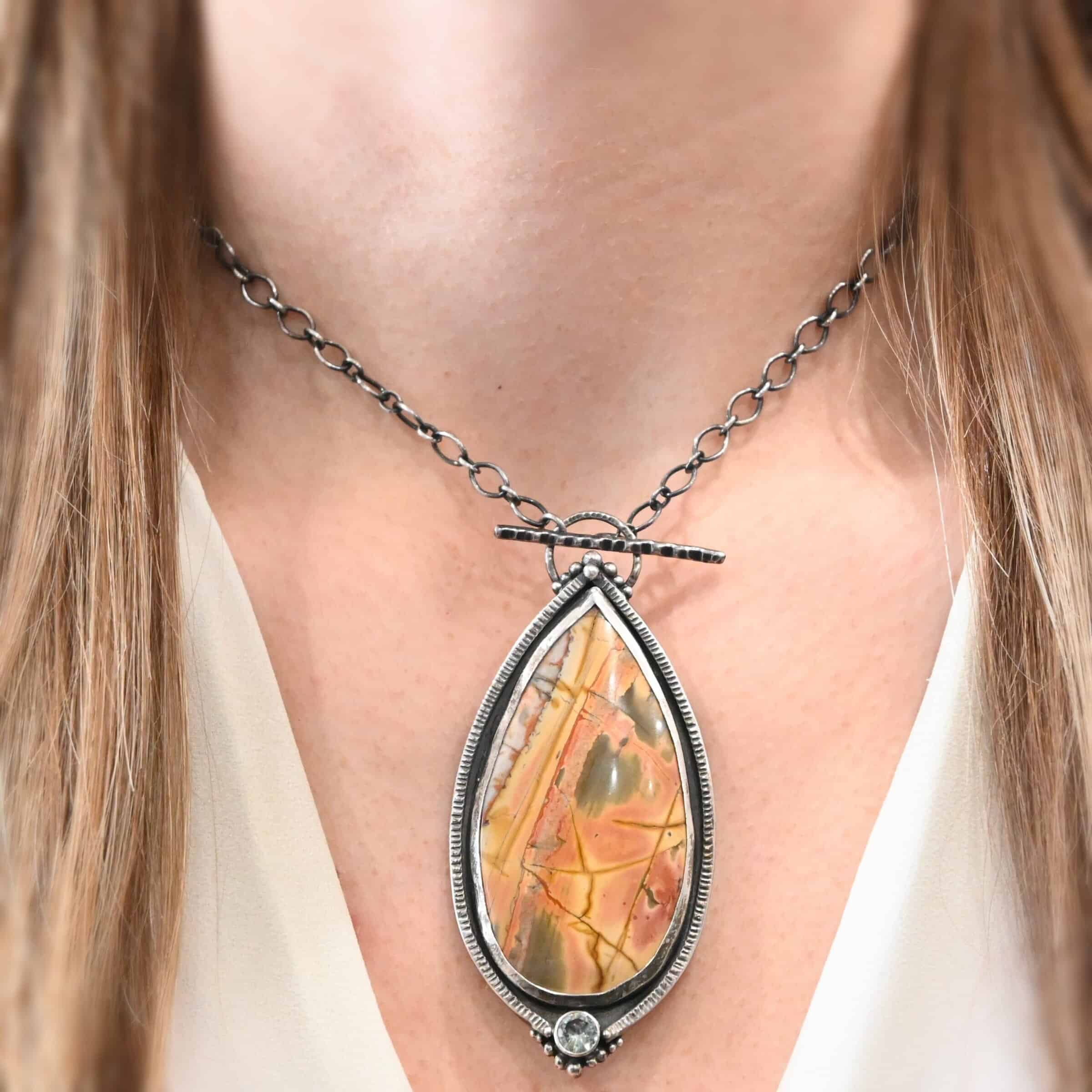 Finding You Necklace "Finding You" Necklace. There is a large, pear shaped cherry creek jasper, pointing upwards. There is a small circular green topaz beneath it, and silver ball detail around that. The silver around the rest of the stone is hammered with lines. There is silver ball detail on the top as well. Necklace is a toggle clasp.