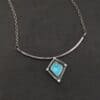 Elsa Necklace "Elsa" Necklace. There is a rough cut apatite in the center of a diamond shaped piece of silver. There is a dot of silver on each point of the silver diamond. The silver diamond is soldered to a curved bar of silver.