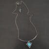 Elsa Necklace "Elsa" Necklace. There is a rough cut apatite in the center of a diamond shaped piece of silver. There is a dot of silver on each point of the silver diamond. The silver diamond is soldered to a curved bar of silver.