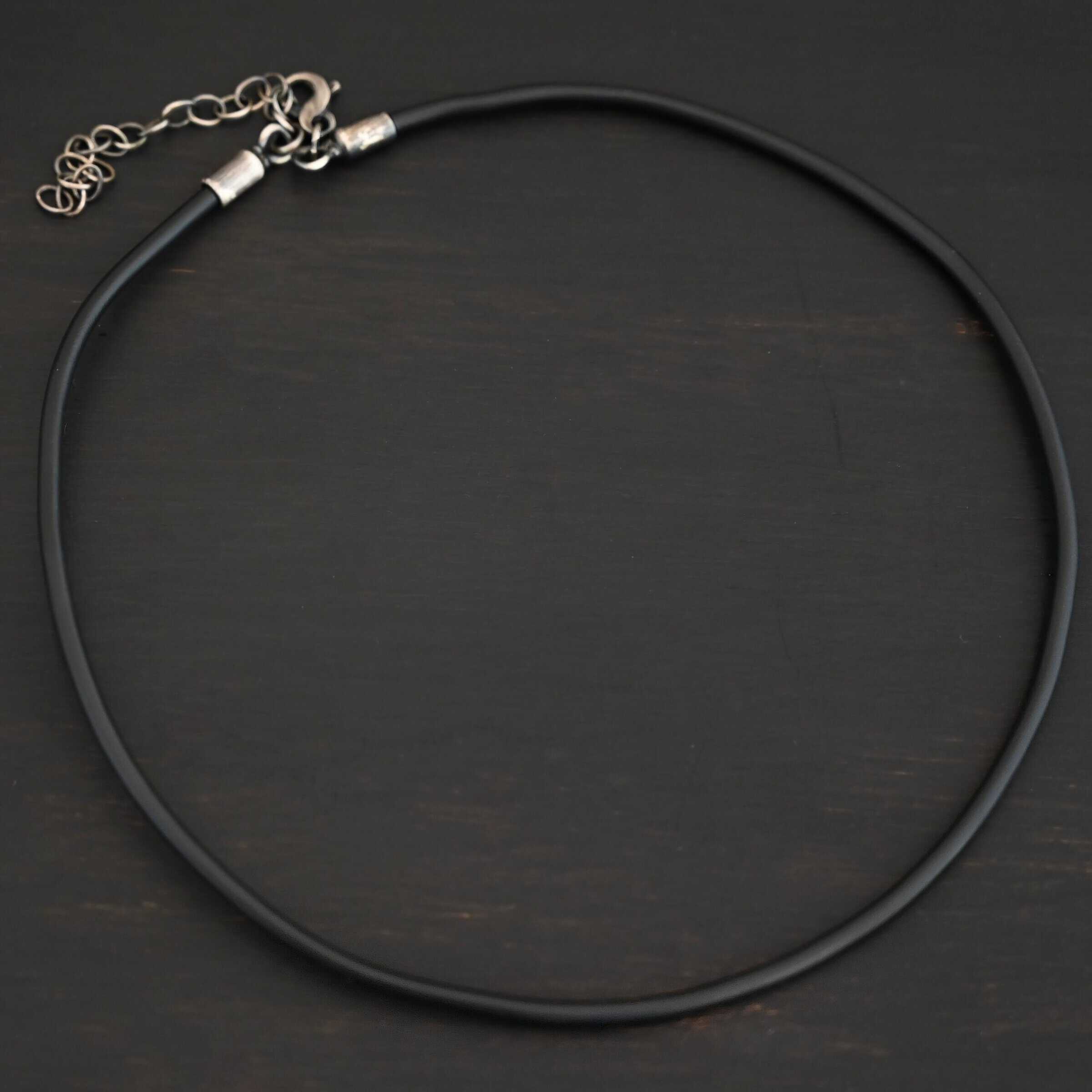 "Wren Wire" Chain. Made out of leather and has sterling silver end caps and a sterling silver chain extension. Chain is shown against a dark background. The leather is black.