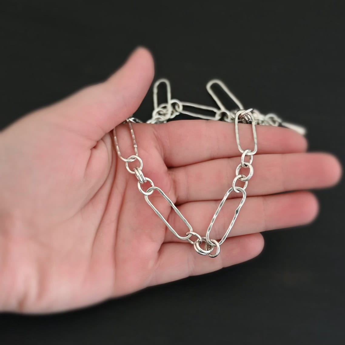 The "Bekah" Chain This chain is handmade out of sterling silver and is shiny. This chain has large oval links that are hammered and connected together by four jump rings. Chain comes with a toggle clasp. The chain is laying on a hand to demonstrate size of the links.