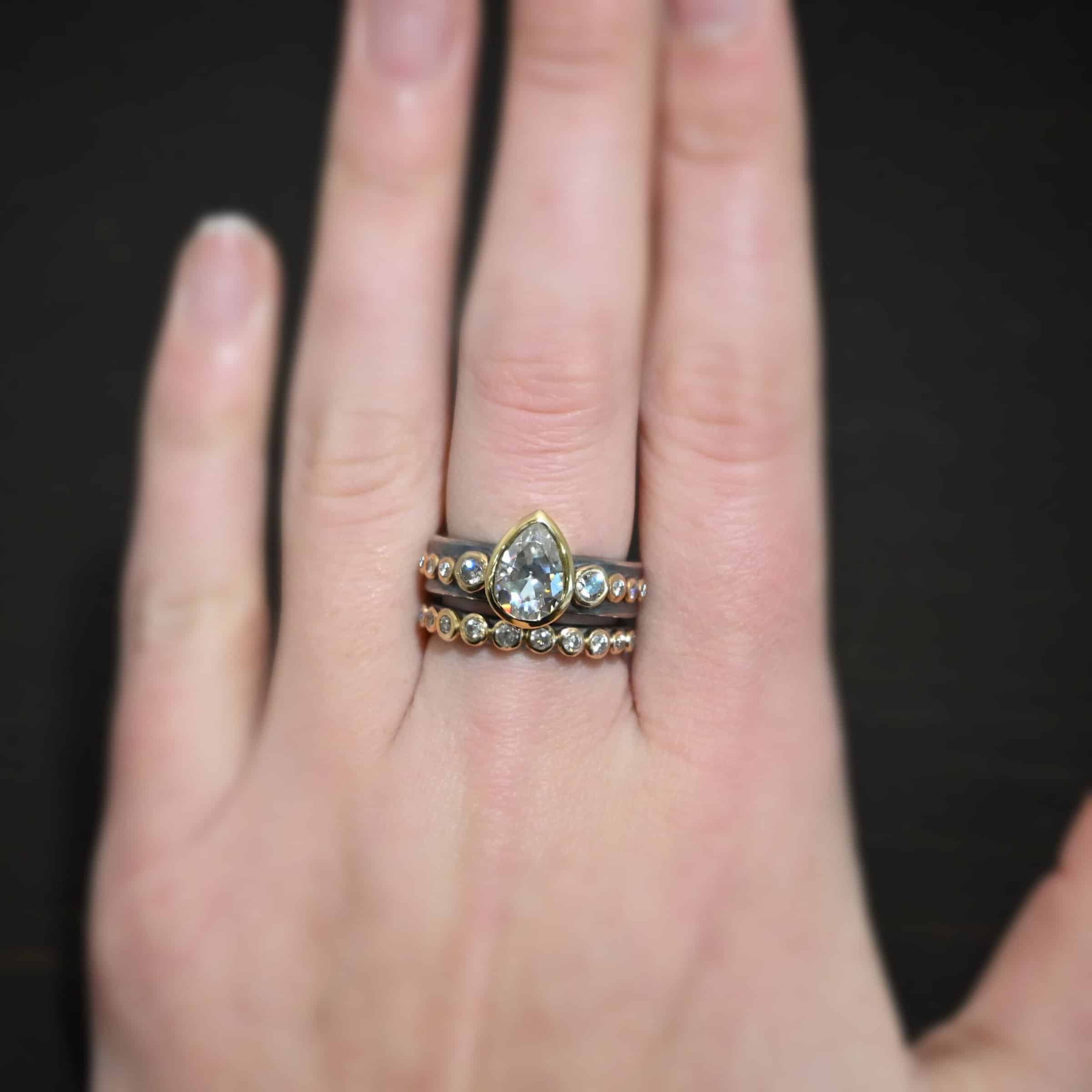 Until Forever Engagement Ring Photo of the "Until Forever" Ring. Made out of sterling silver and moissanites. The center moissanite is a pear shape. There are 17 other moissanites that go straight around the top and bottom band. Eight of them are on the top band, four on each side of the pear moissanite. Bands are worn on a models middle finger to demonstrate size.