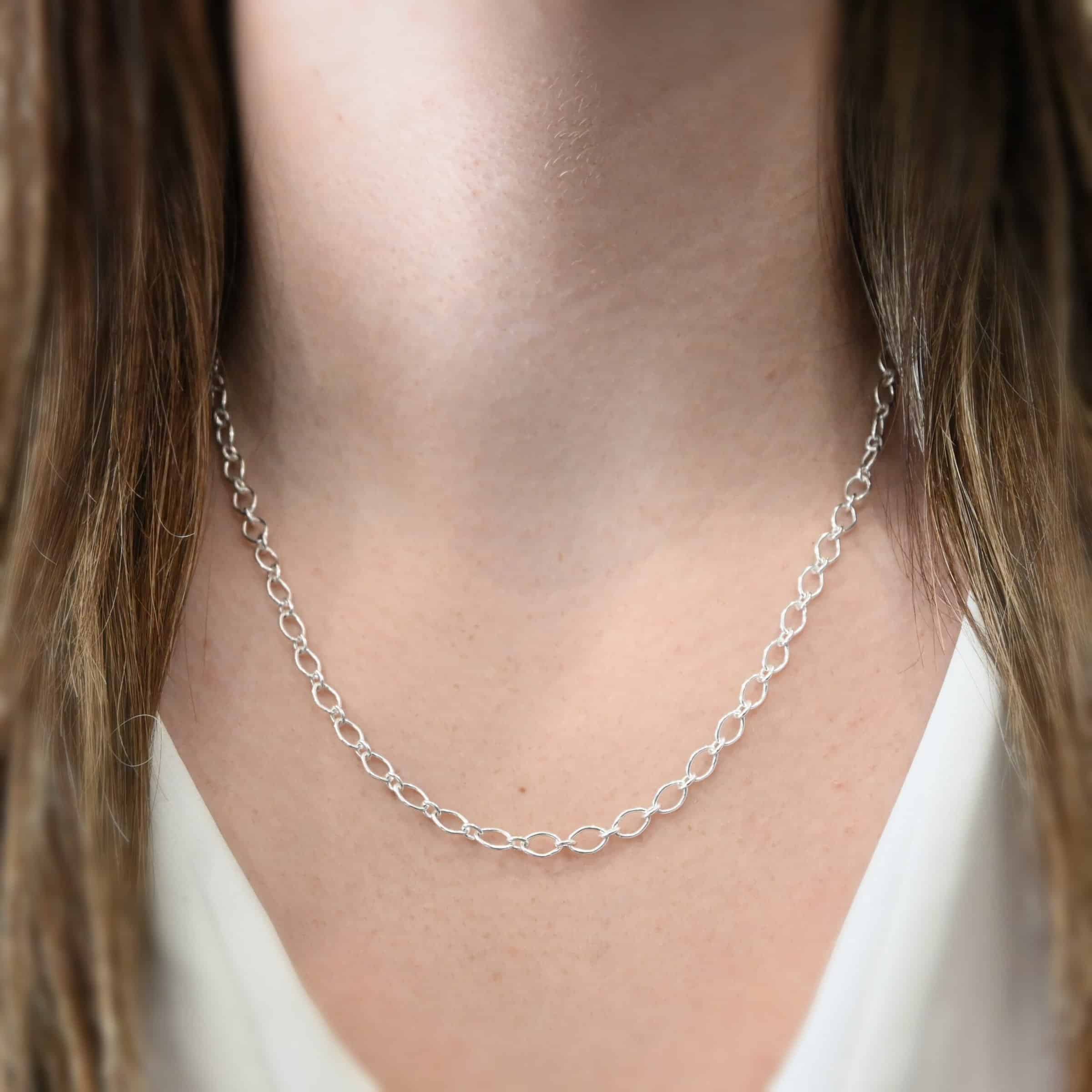 Allie Chain 20” Shiny Close up of the "Allie" Chain worn on a model. Links measure 7×4.6mm. Chain is shown at 20" long and shiny on a model. Model is wearing a white v-neck shirt.