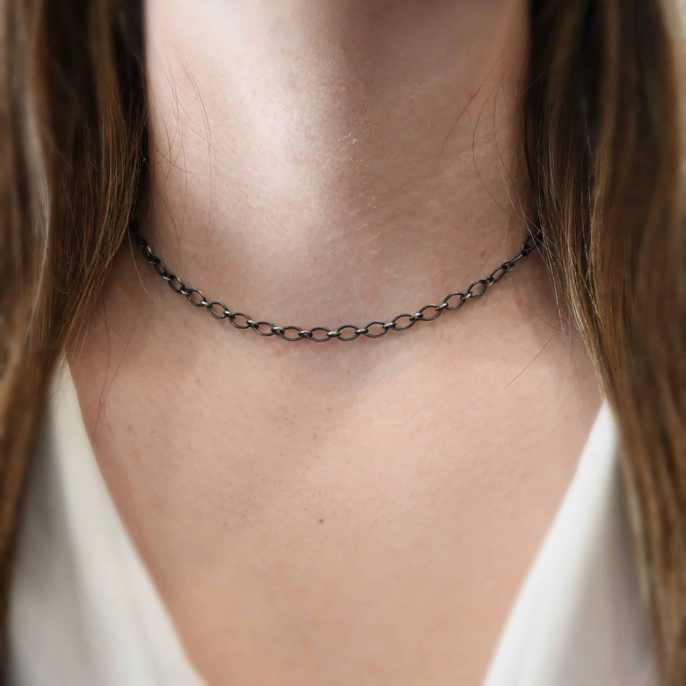 Allie Chain 16” Oxidized Close up of the "Allie" Chain worn on a model. Links measure 7×4.6mm. Chain is shown at 16" long and oxidized on a model. Model is wearing a white v-neck shirt.